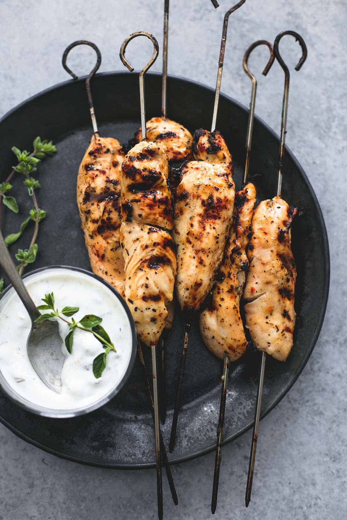 top view of grilled chicken Souvlaki on skewers & Tzatziki sauce on a plate.