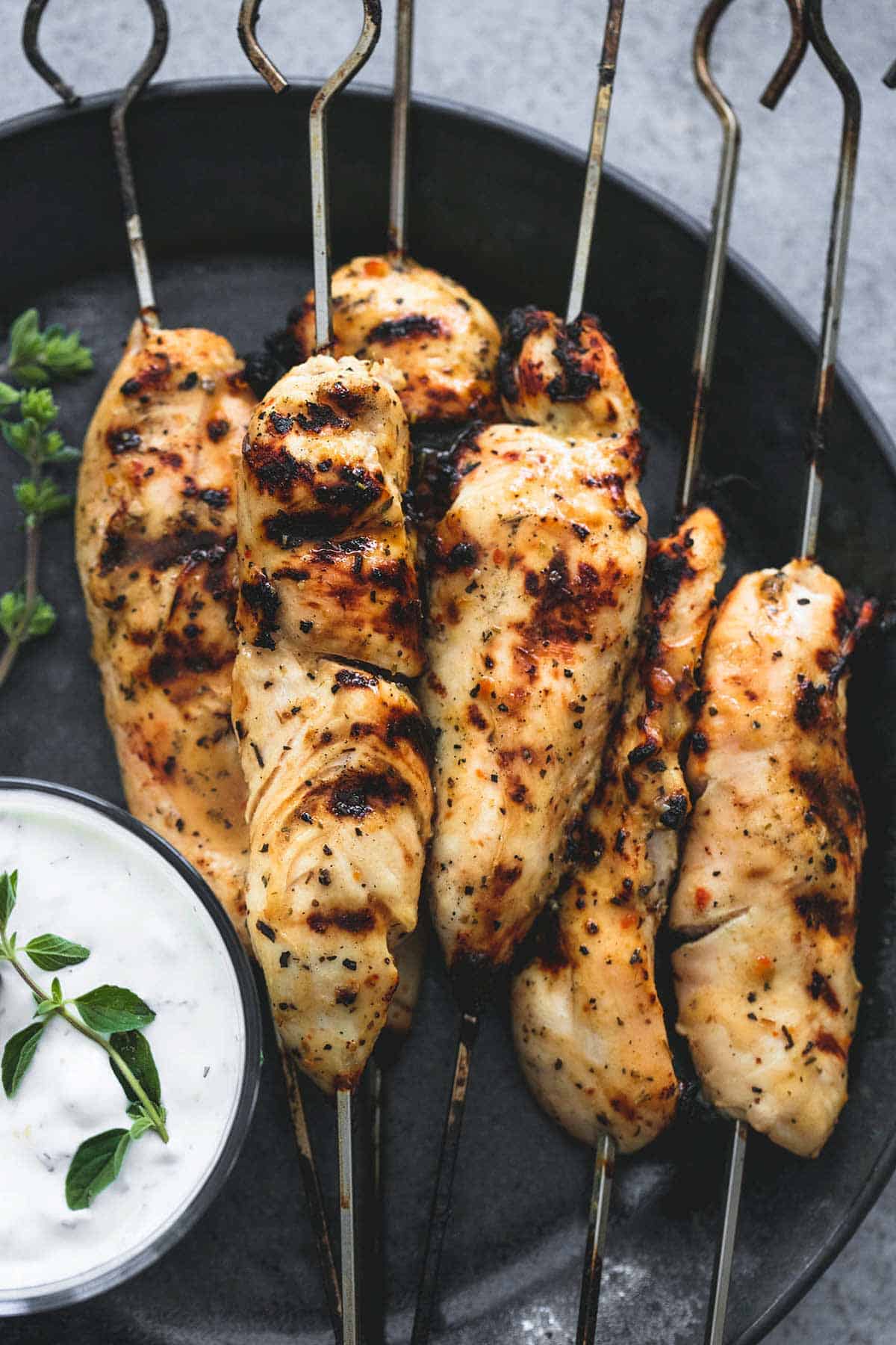 close up top view of grilled chicken Souvlaki on skewers & Tzatziki sauce on a plate.