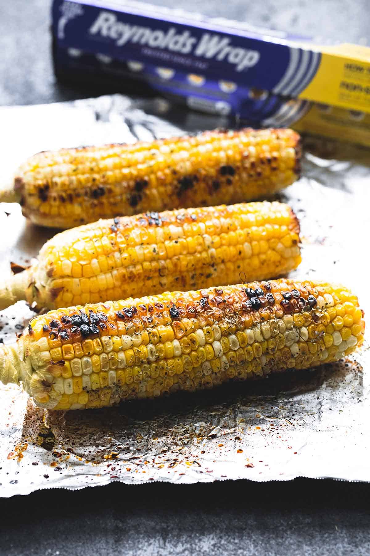 grilled corn on the cobs on aluminum foil with the box of aluminum foil in the background.