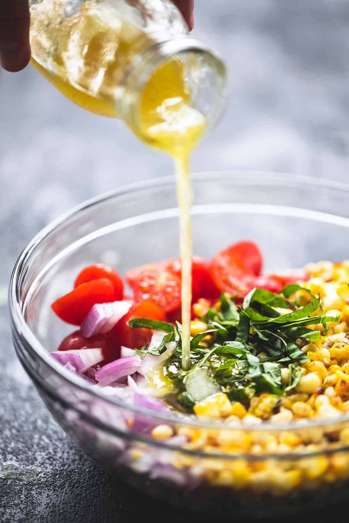 dressing being poured on top of grilled corn salad not yet tossed in a bowl.