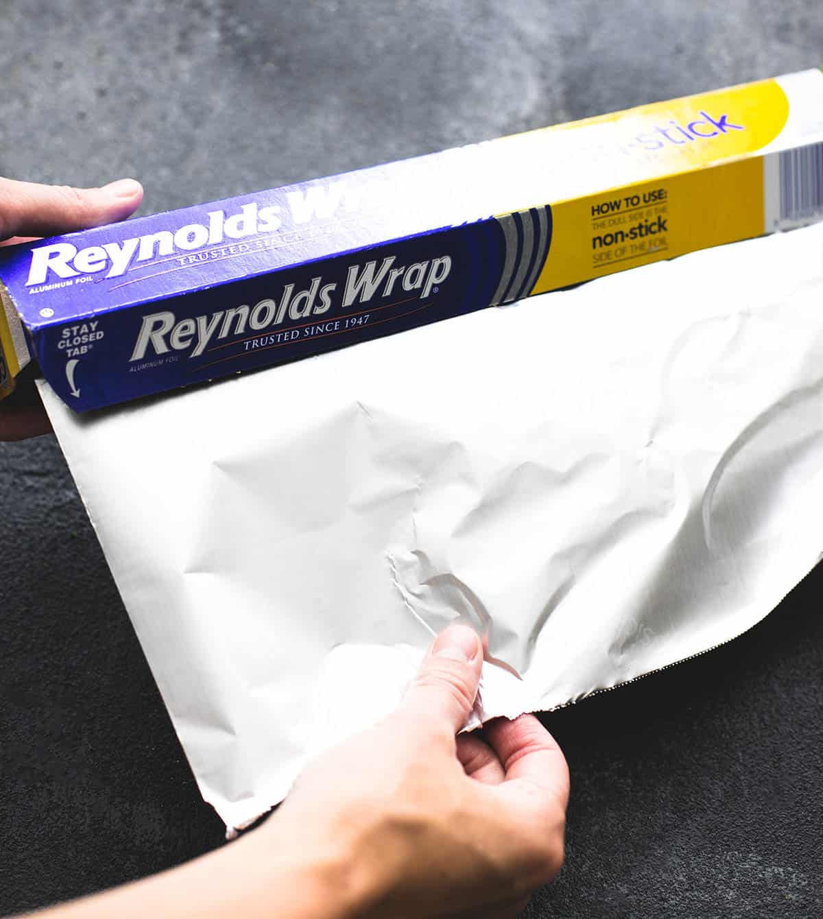 a hand pulling out aluminum foil from a box.