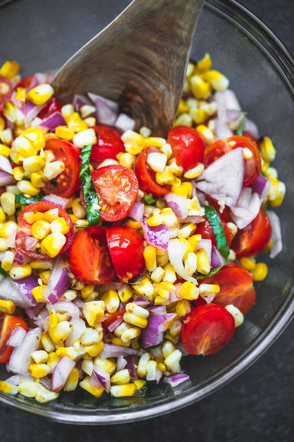 close up top view of grilled corn salad with a wooden serving spoon in a bowl.