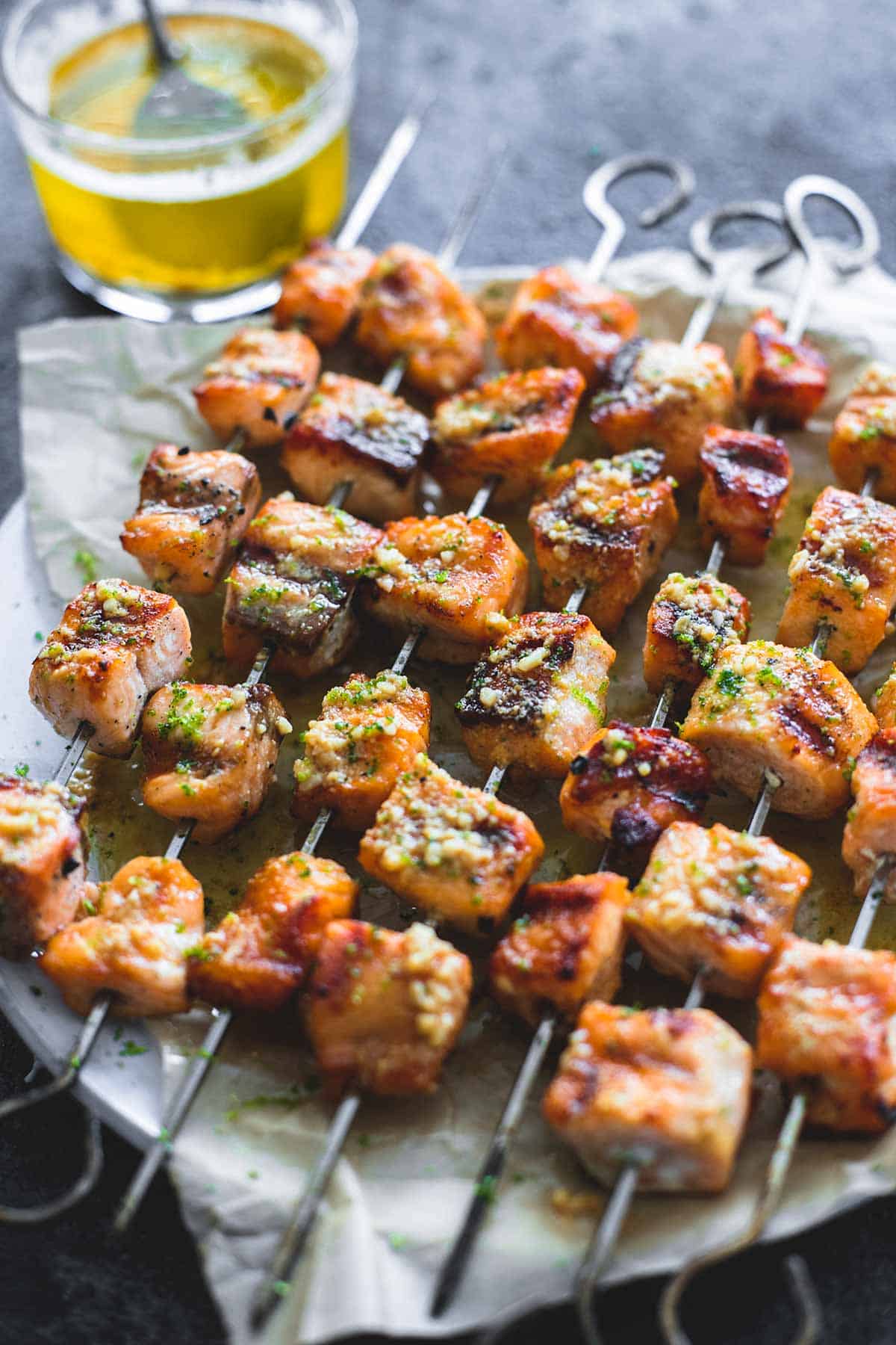 grilled lime butter salmon skewers on a plate with butter sauce and a spoon in a glass in the background.