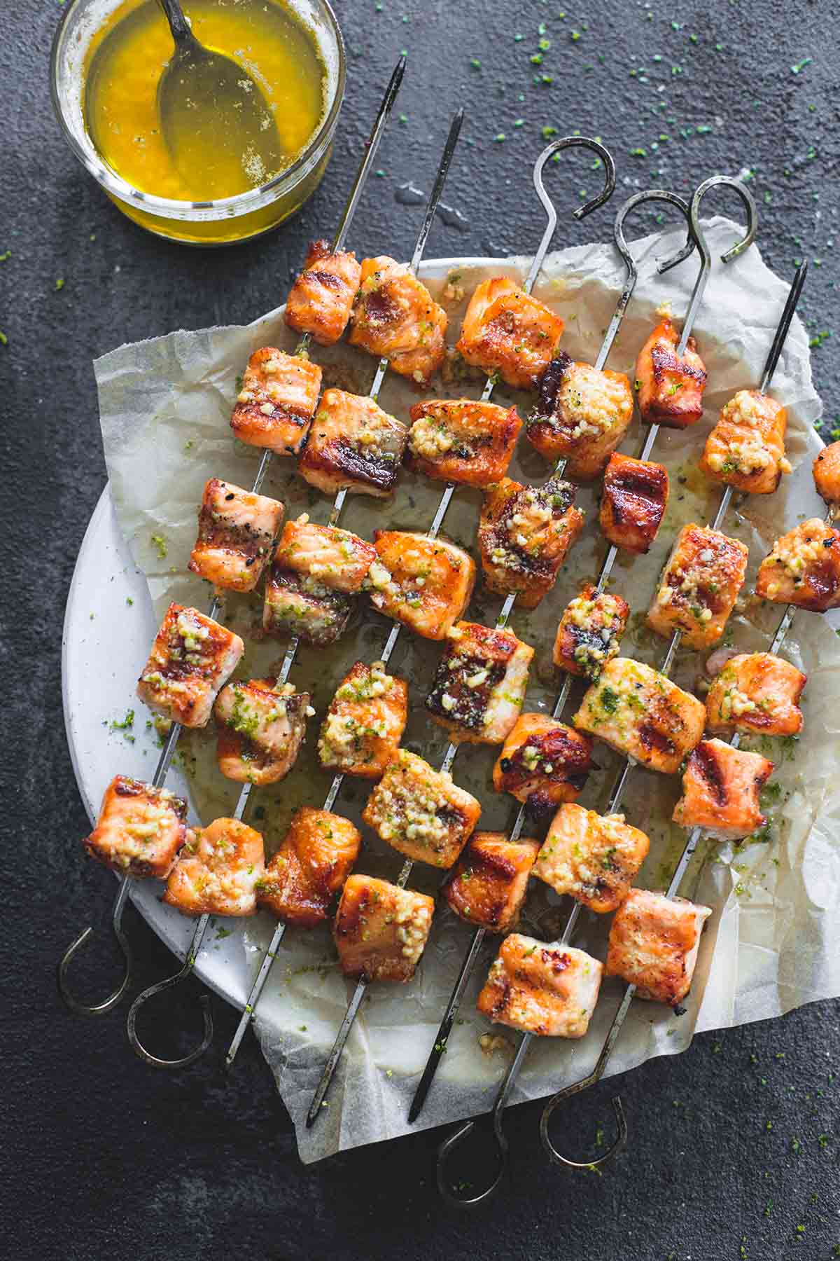 top view of grilled lime butter salmon skewers on a plate with butter sauce and a spoon in a glass on the side.