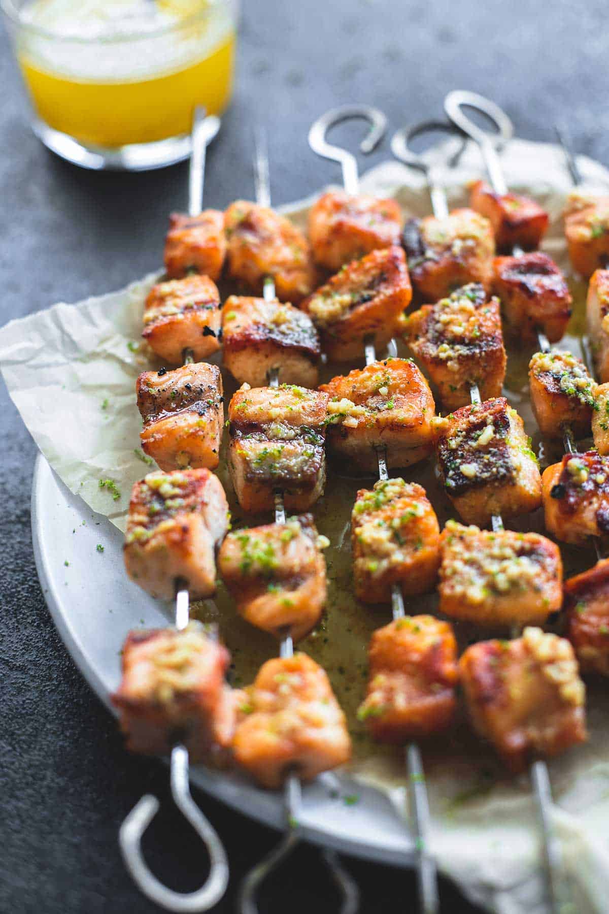 grilled lime butter salmon skewers on a plate with a glass of butter sauce in the background.