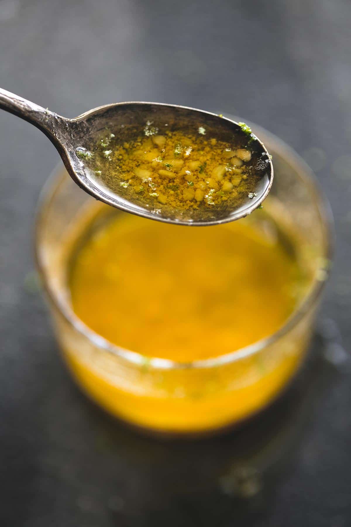 a spoon with butter sauce lifted up above a glass of melted butter sauce.