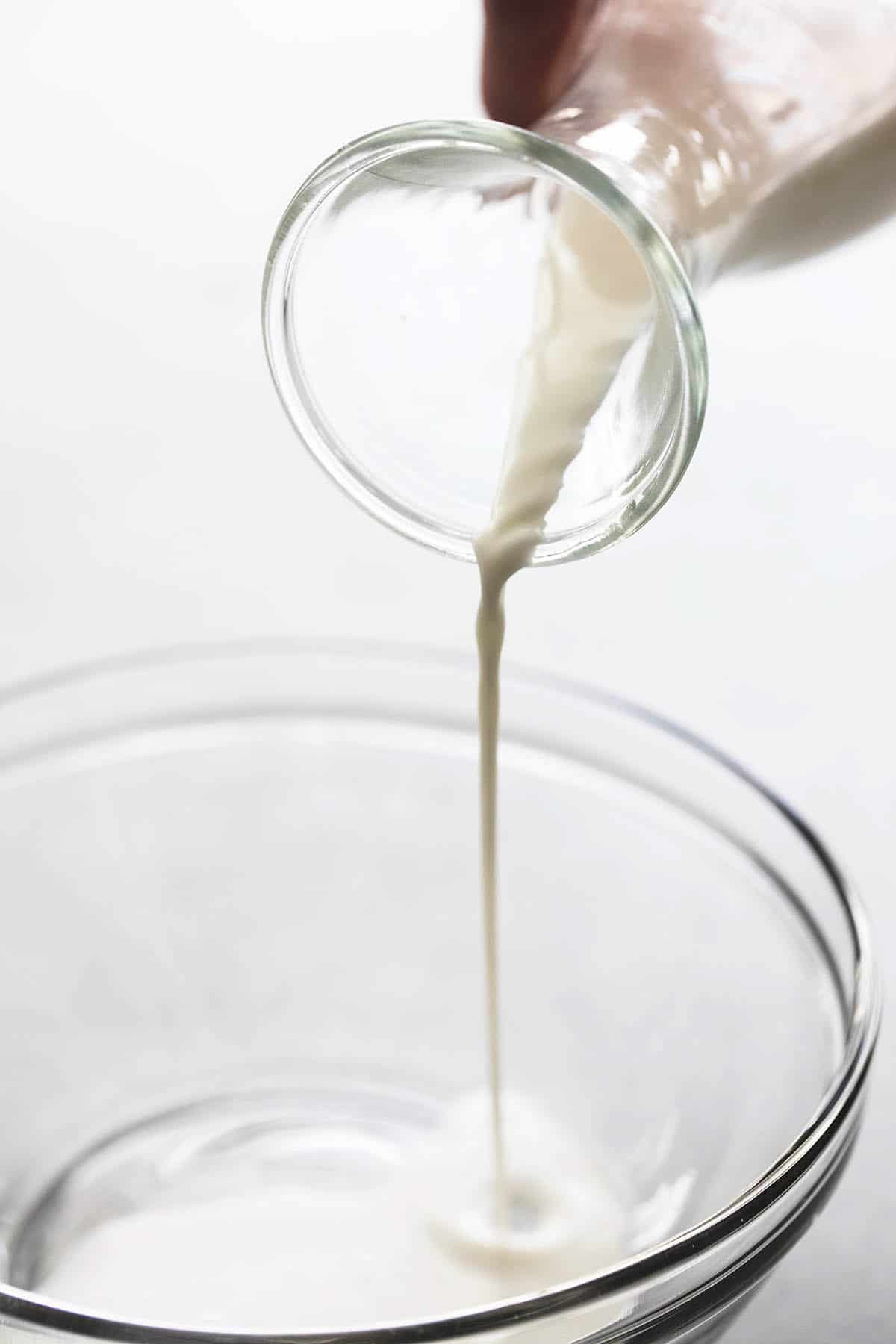 milk being poured into a glass bowl from a carafe.