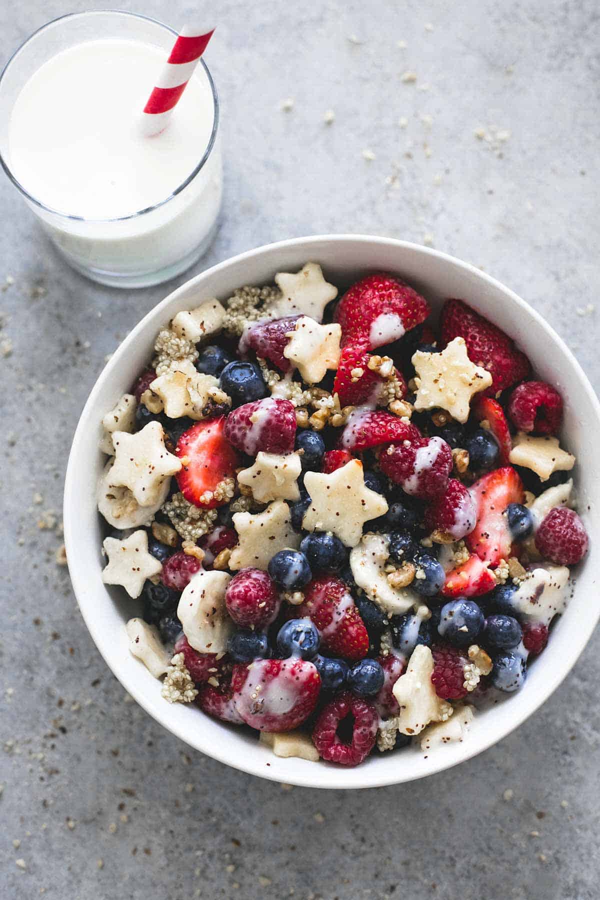 close up of Patriotic fruit salad with honey lime dressing in a bowl with a glass of milk with a straw on the side.