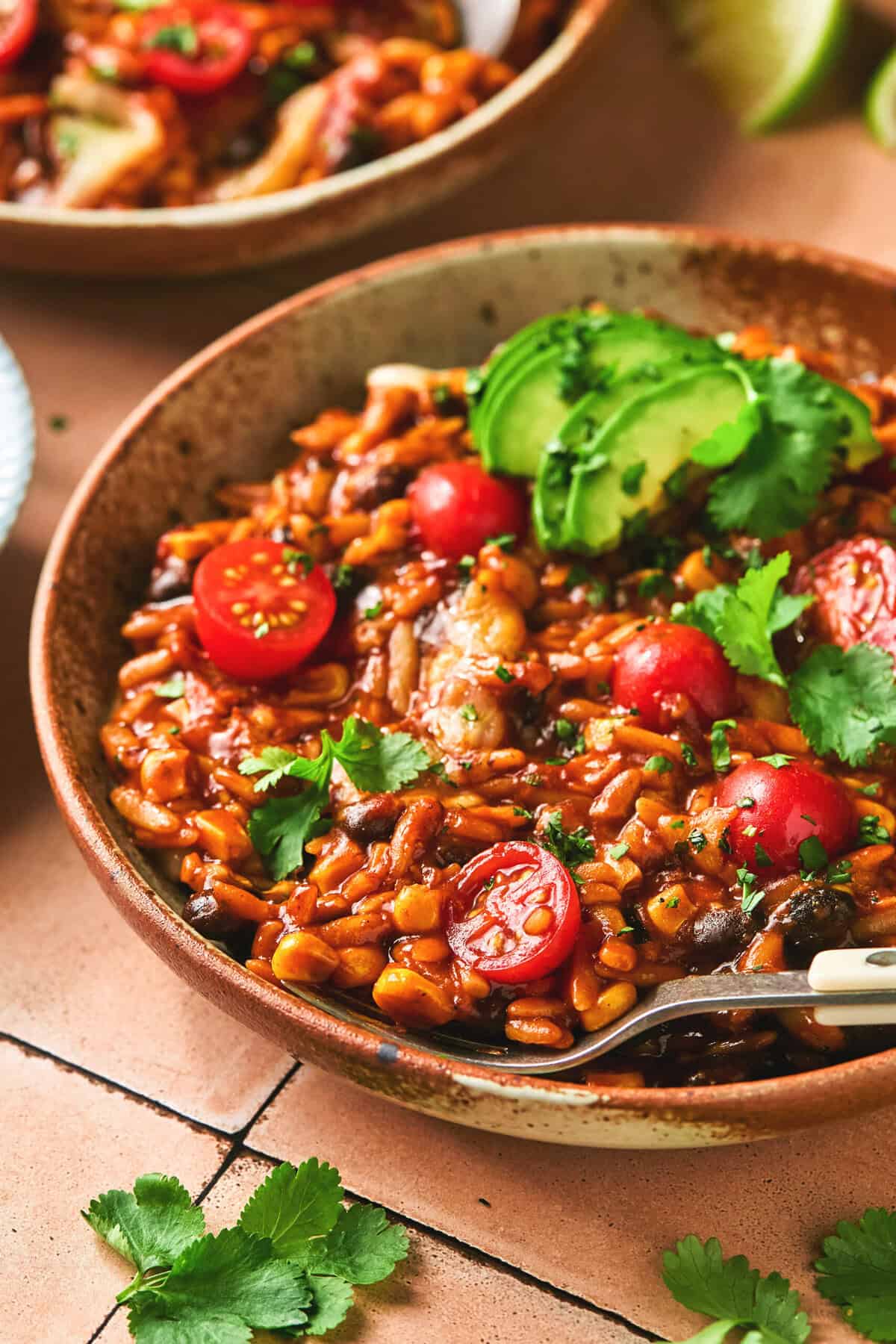 bowl of saucy orzo with cheese, cilantro, and tomatoes with fork.