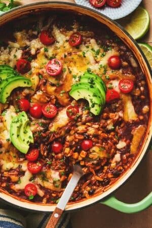 cheesy enchilada orzo pasta with serving spoon in cast iron pan.