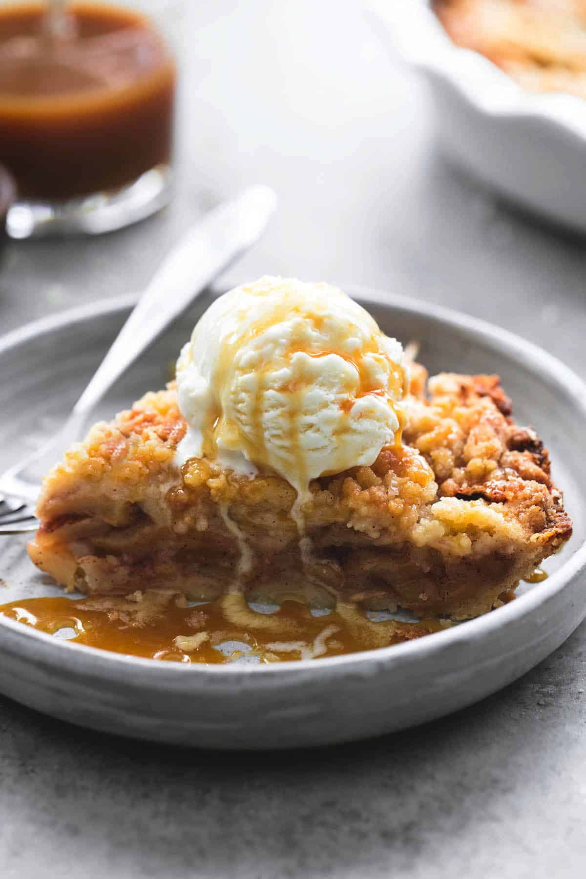 a piece of apple crumble pie topped with vanilla ice cream and caramel sauce with a fork on a plate.