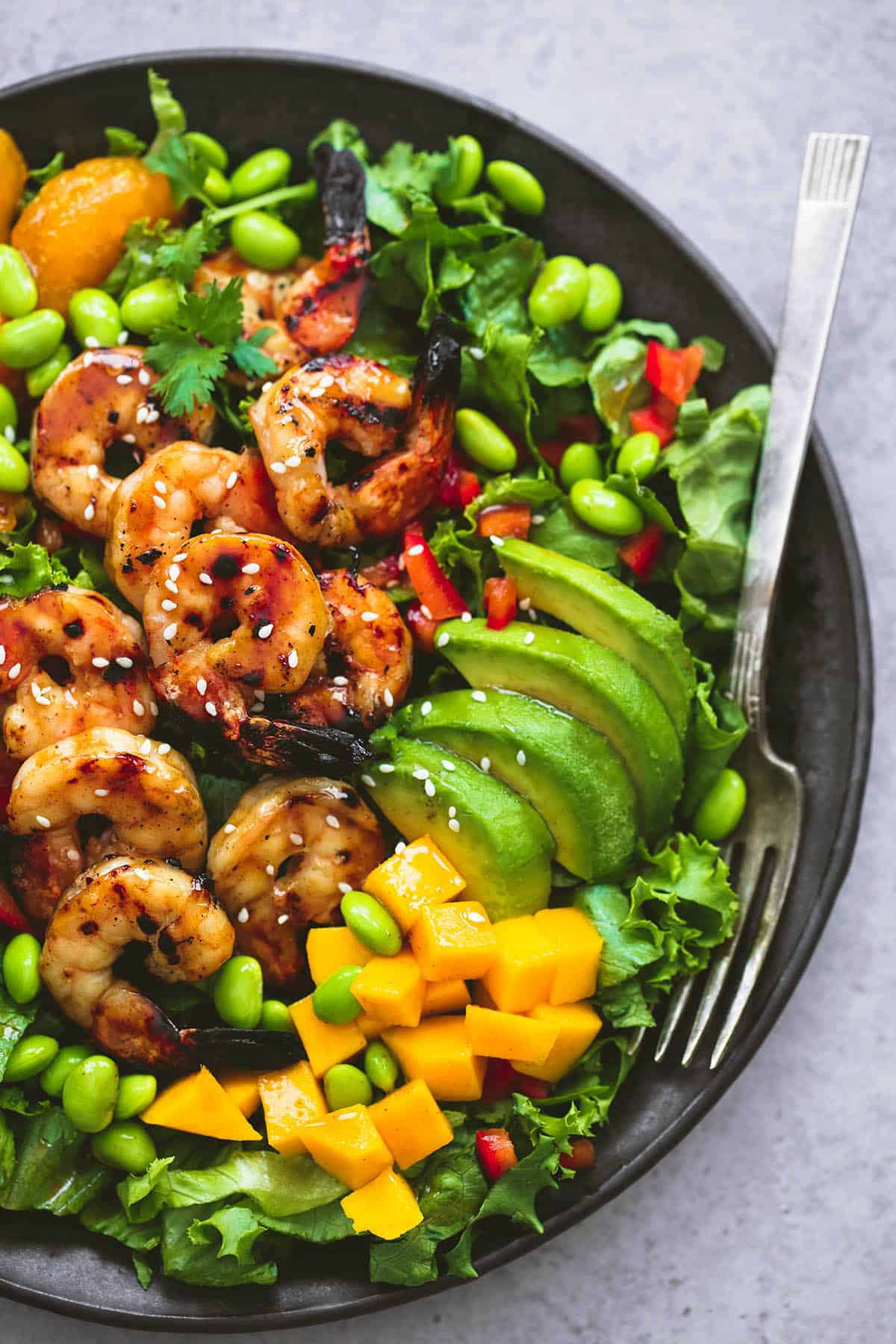 top view of mango mandarin sesame shrimp salad and a fork on a plate.