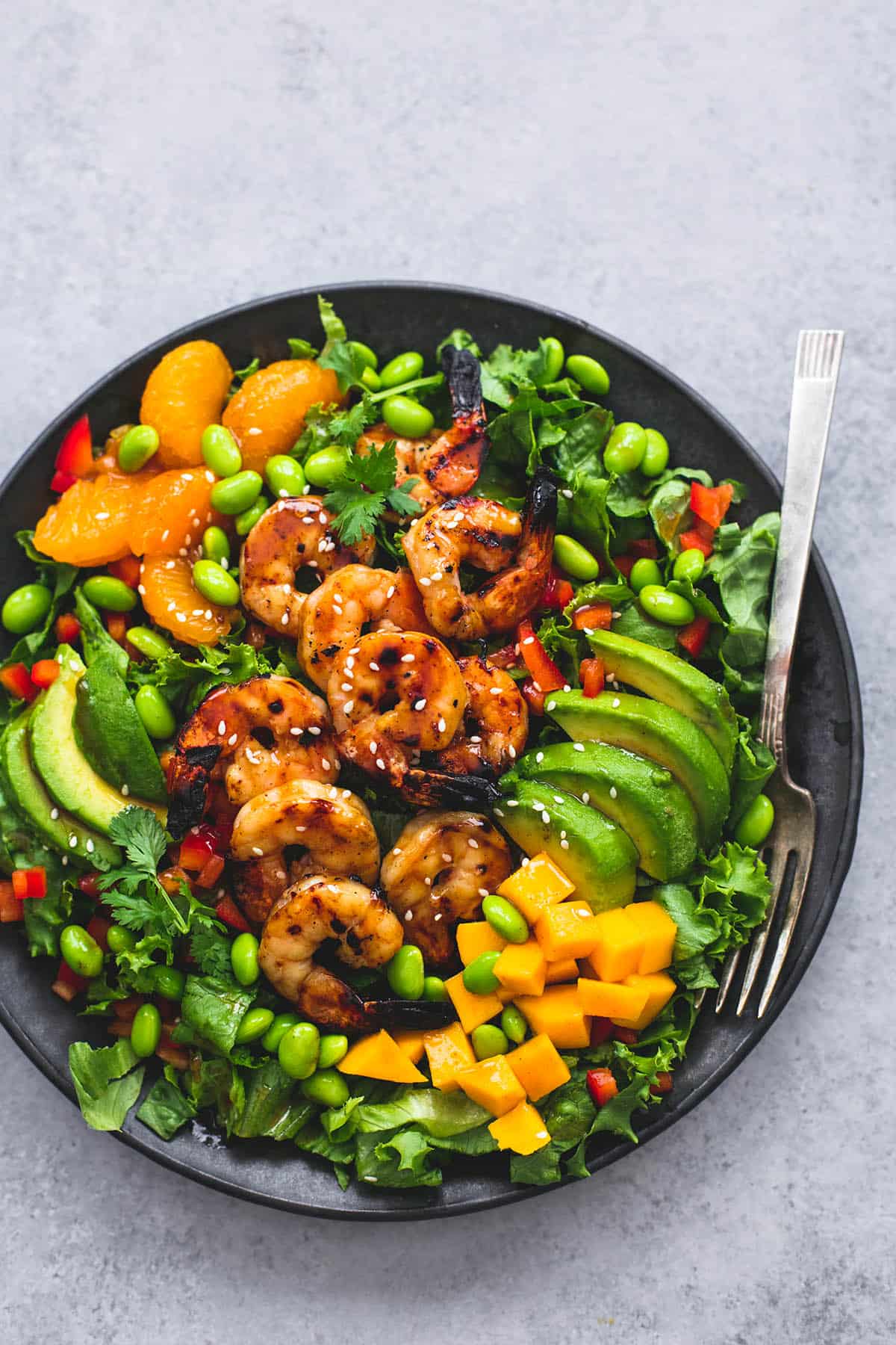 top view of mango mandarin sesame shrimp salad with a fork on a plate.
