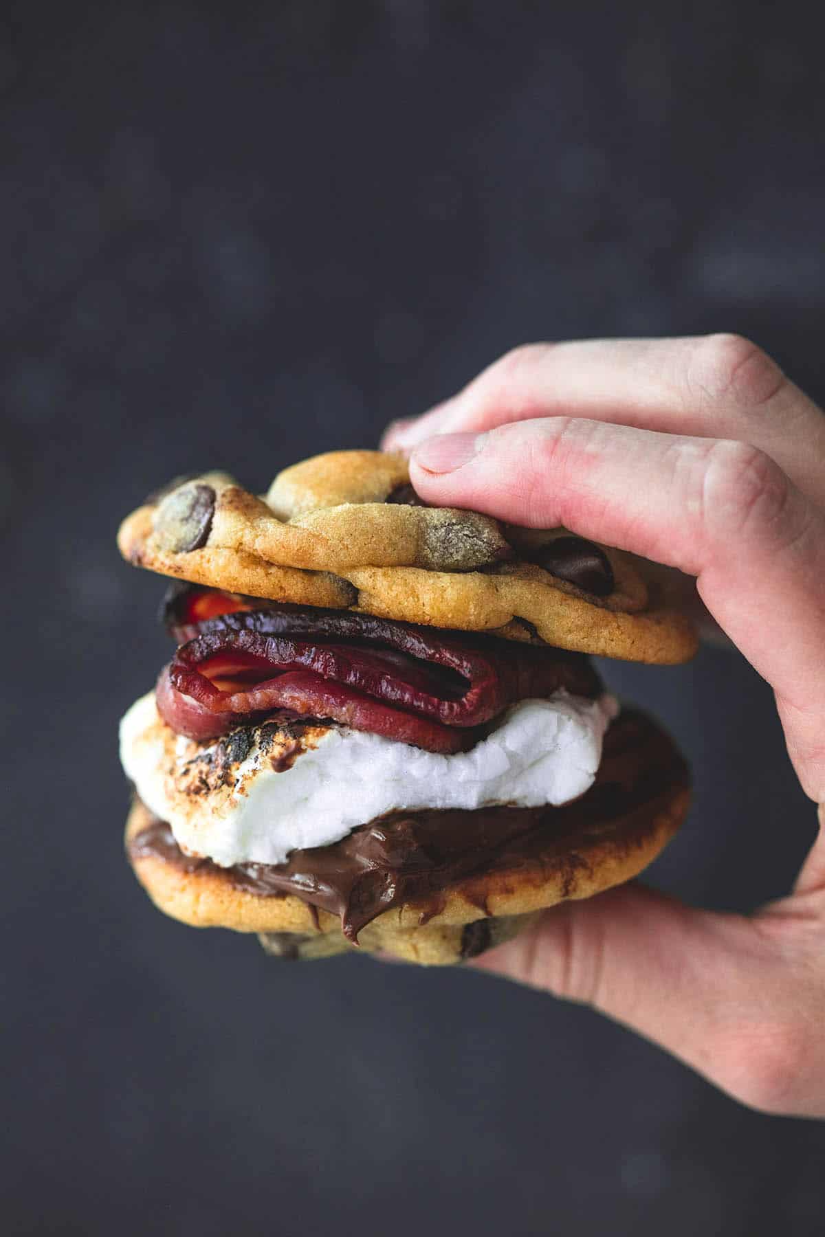 a hand holding a grilled chocolate chip cookie bacon S'more.