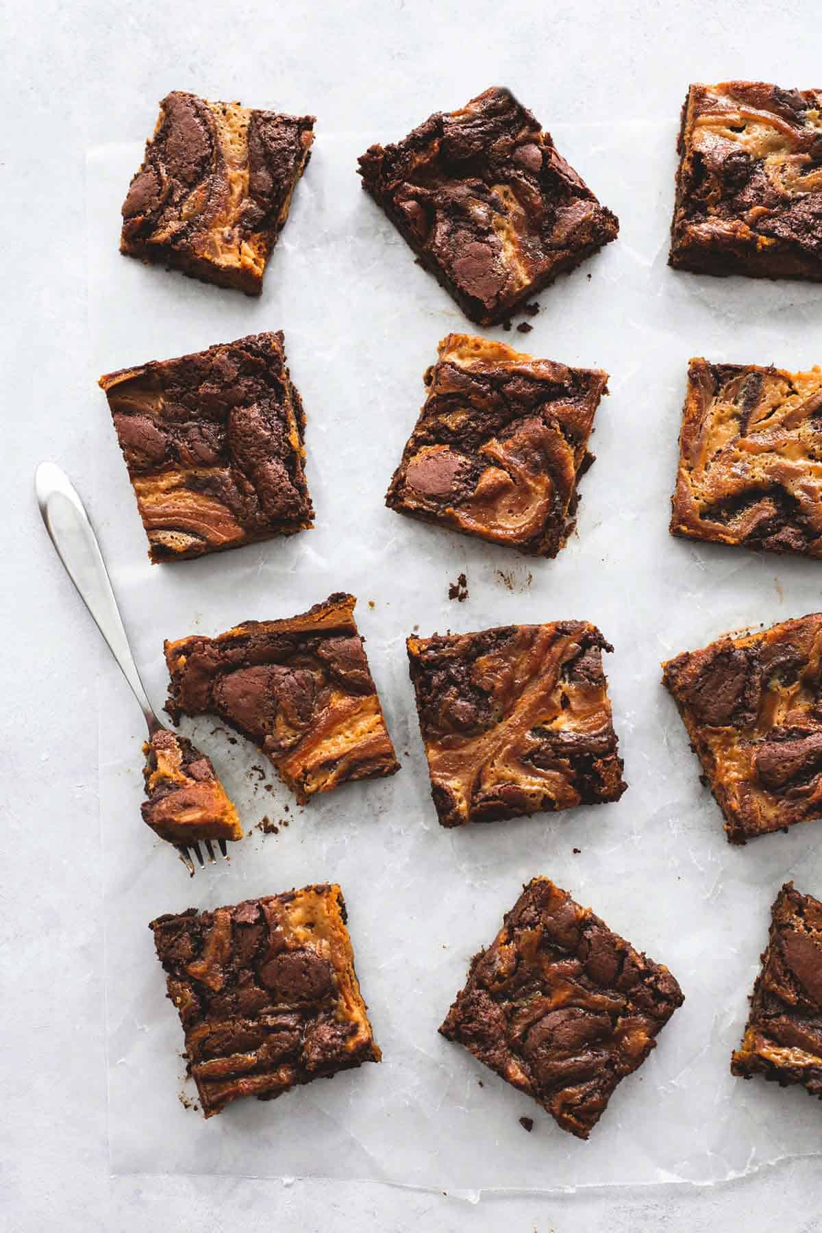 top view of gooey caramel pumpkin brownies in a vertical lines with one brownie having a bite on a fork on the side.