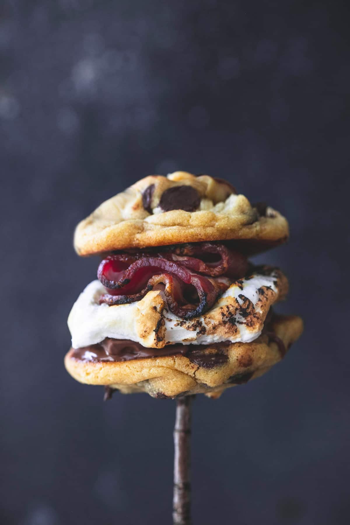 a grilled chocolate chip cookie bacon S'more on a roasting stick.