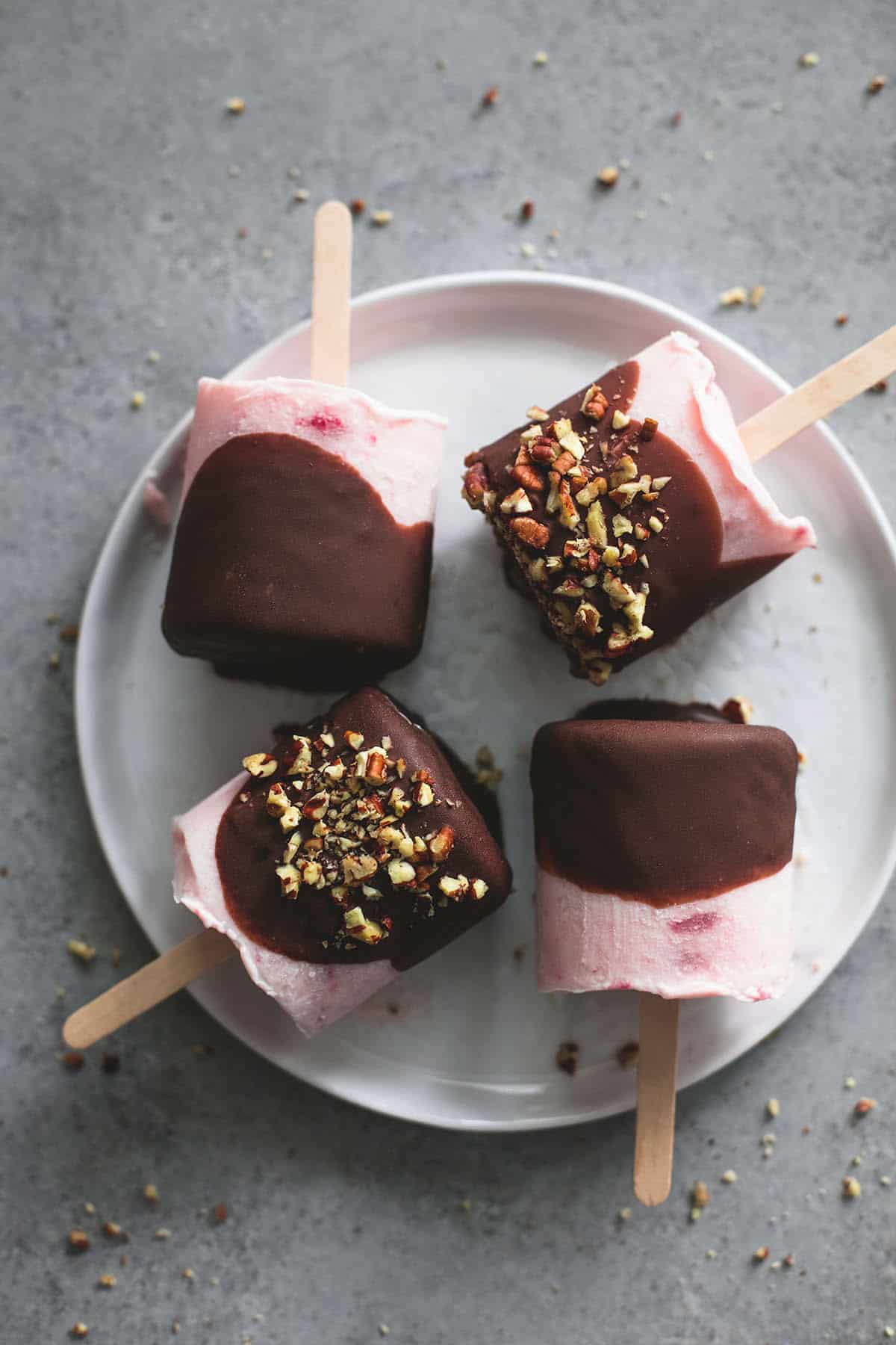 top view of chocolate covered strawberry yogurt pops with some topped with crushed pecans on a plate.