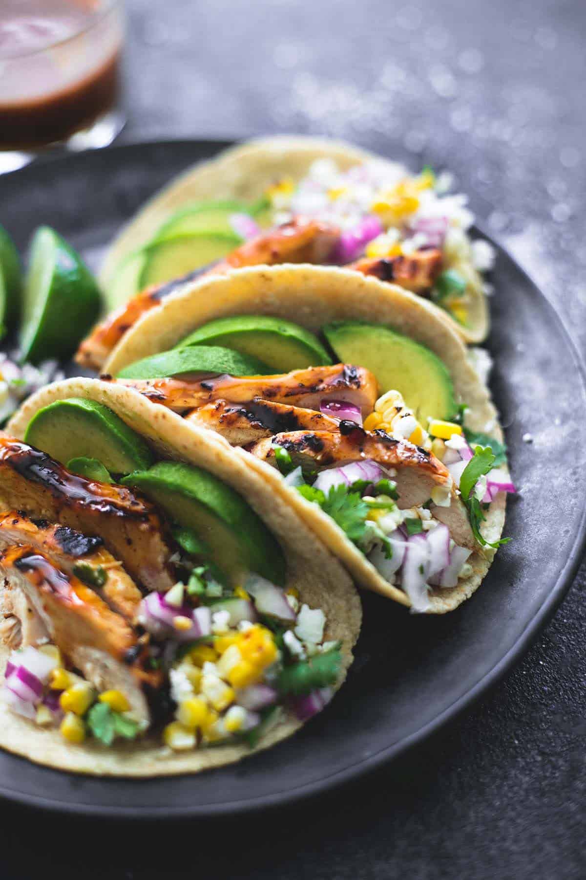 grilled chicken tacos with lime slices on the side on a platter with marinade in a glass in the background.