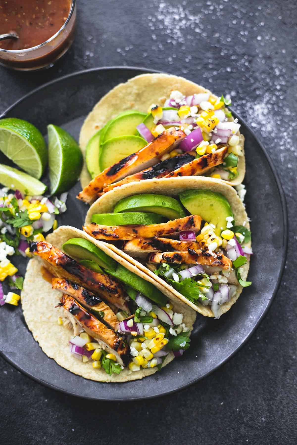 top view of grilled chicken tacos with lime slices on the side on a plate with marinade and a spoon in a glass.