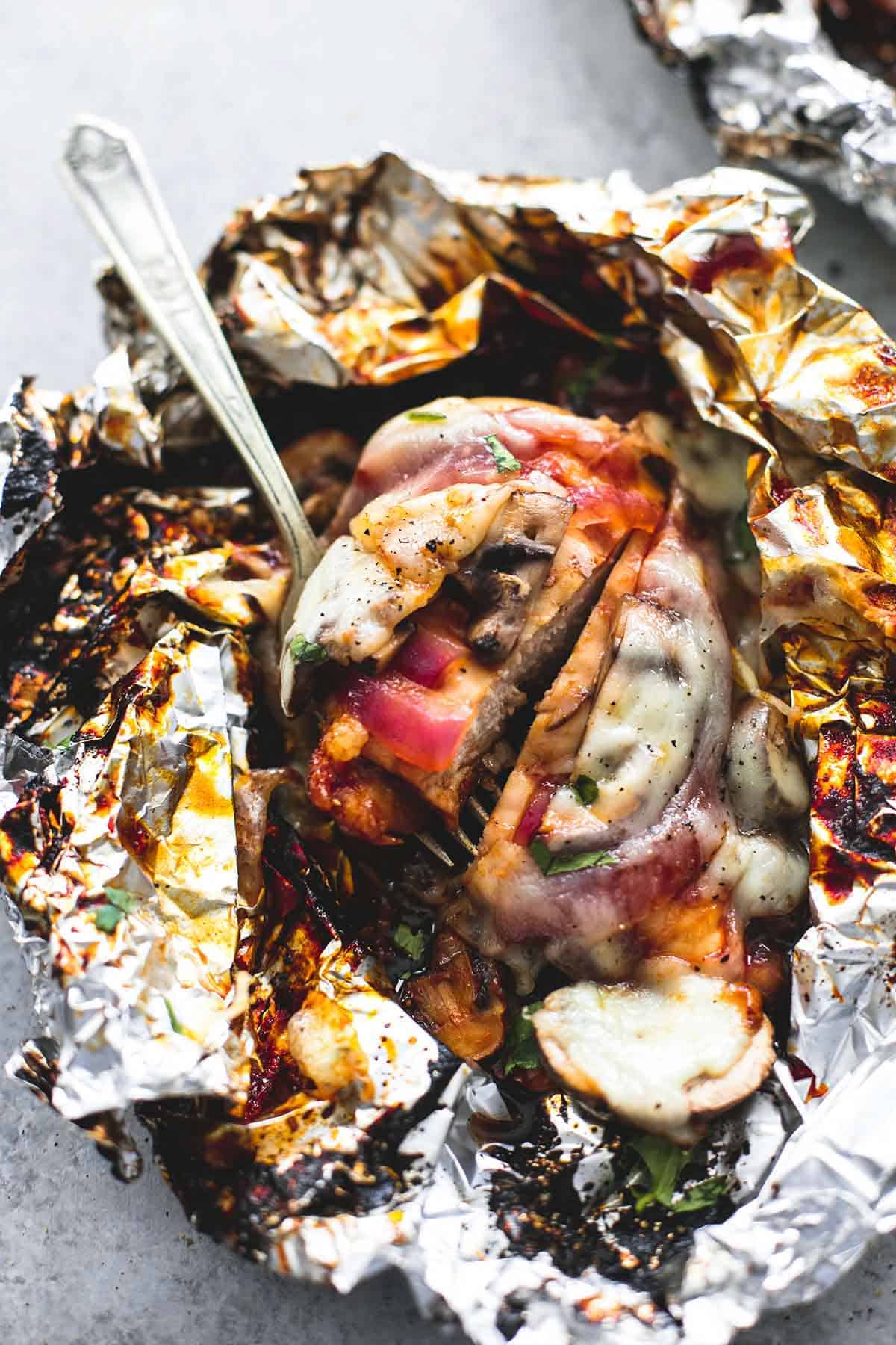 close up top view of a grilled smothered bbq chicken foil pack with a fork.