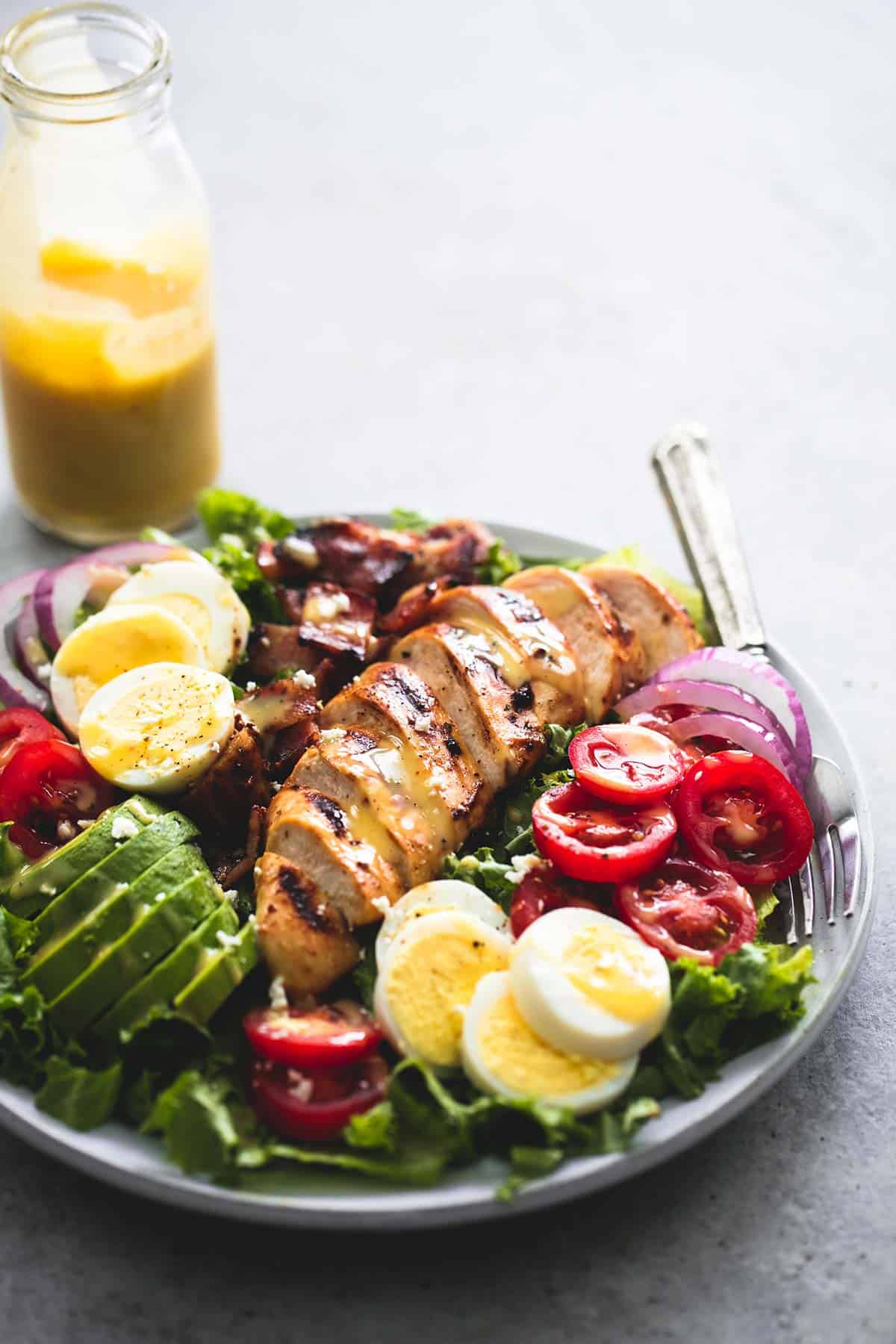 honey mustard chicken cobb salad with a fork on a plate with a jar of dressing on the side.