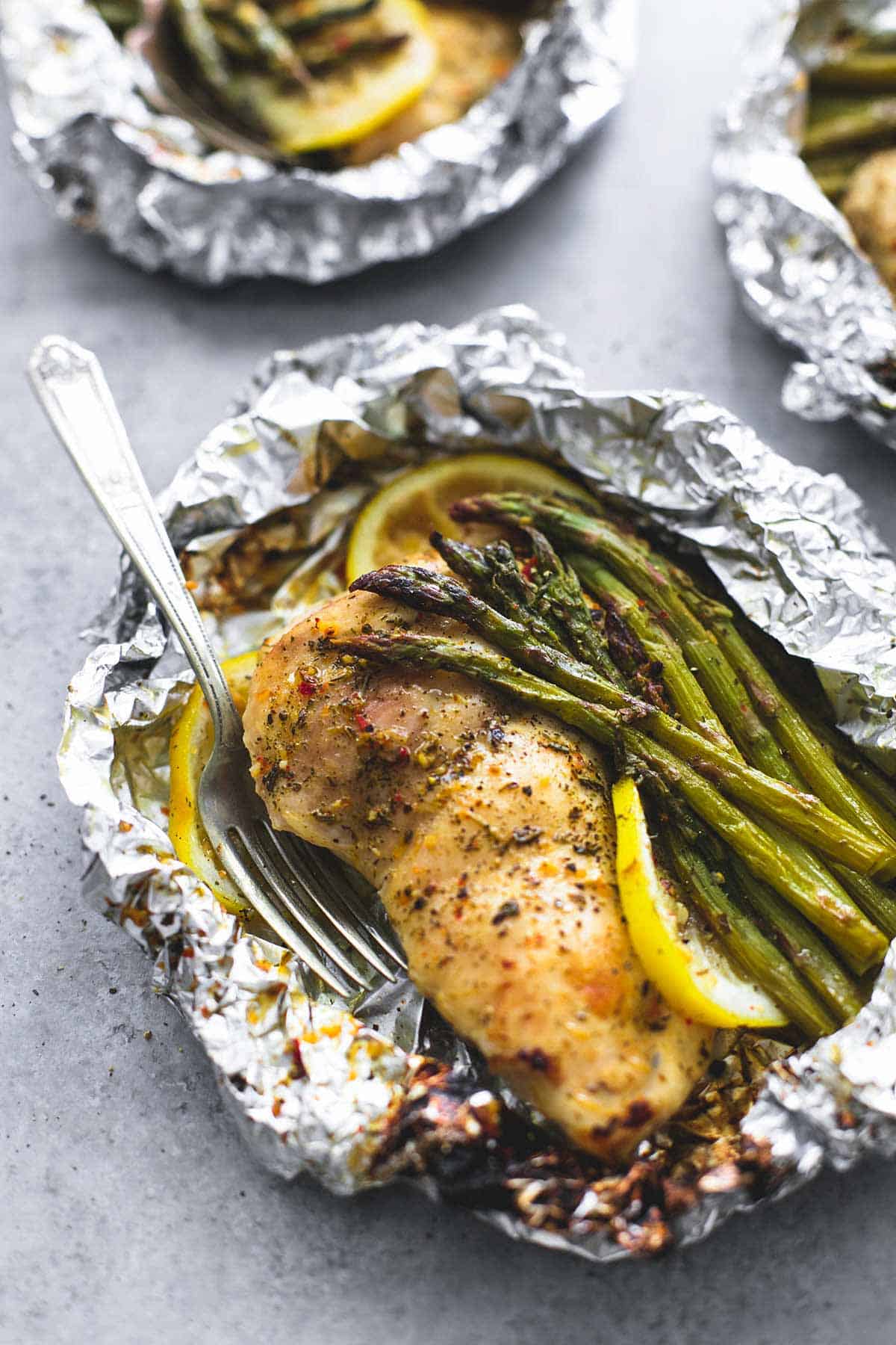 a lemon chicken & asparagus foil pack with a fork with more foil packs in the background.