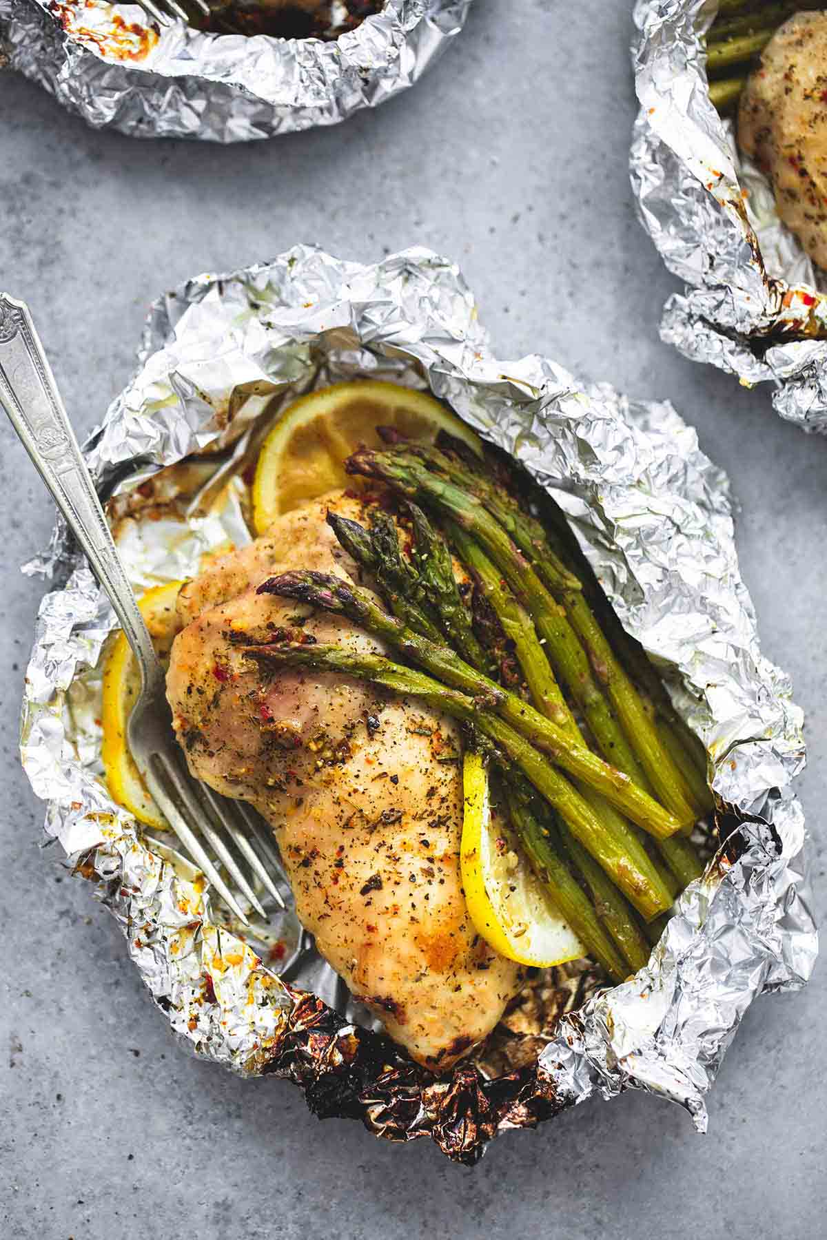 top view of a lemon chicken & asparagus foil pack with a fork with more foil packs on the side.
