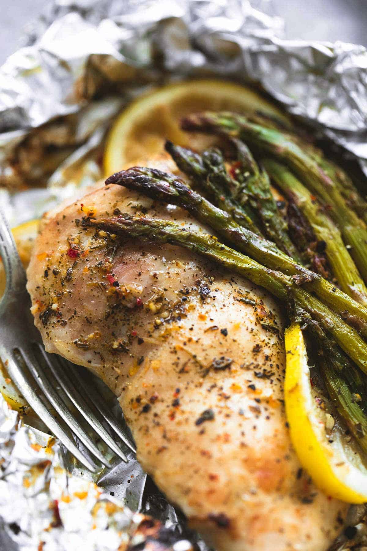 close up of a lemon chicken & asparagus foil pack with a fork.