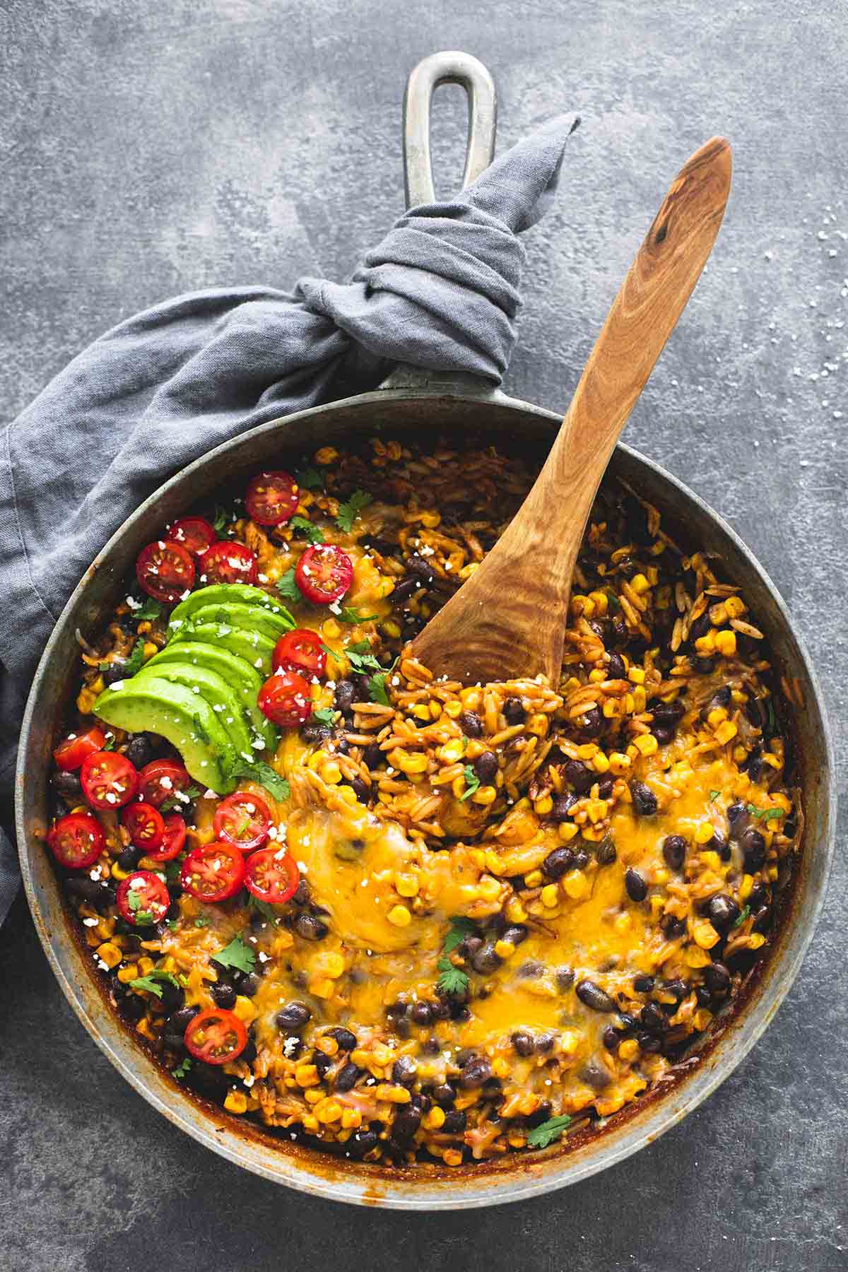 top view of enchilada orzo with avocado slices, and a wooden serving spoon in a pan.