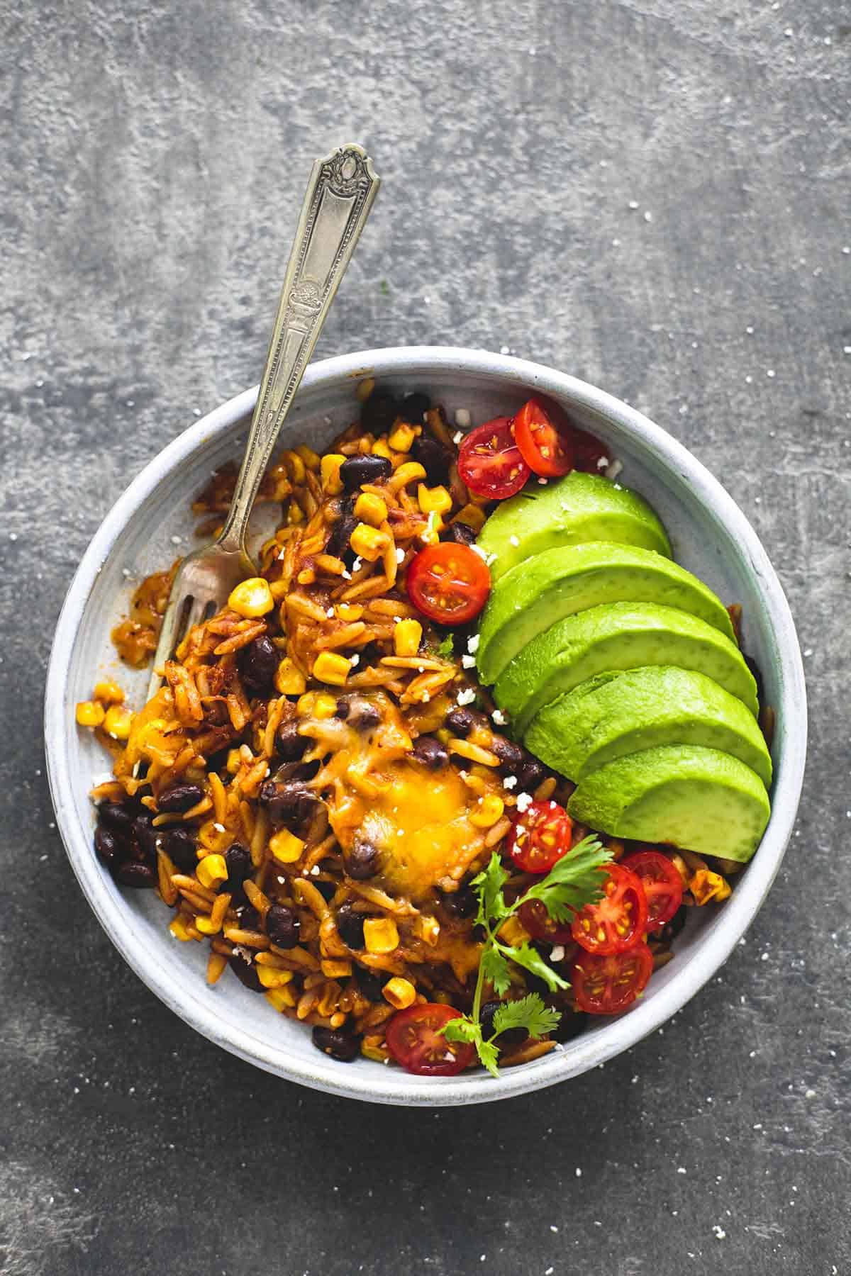 top view of enchilada orzo with avocado slices and a fork on a plate.