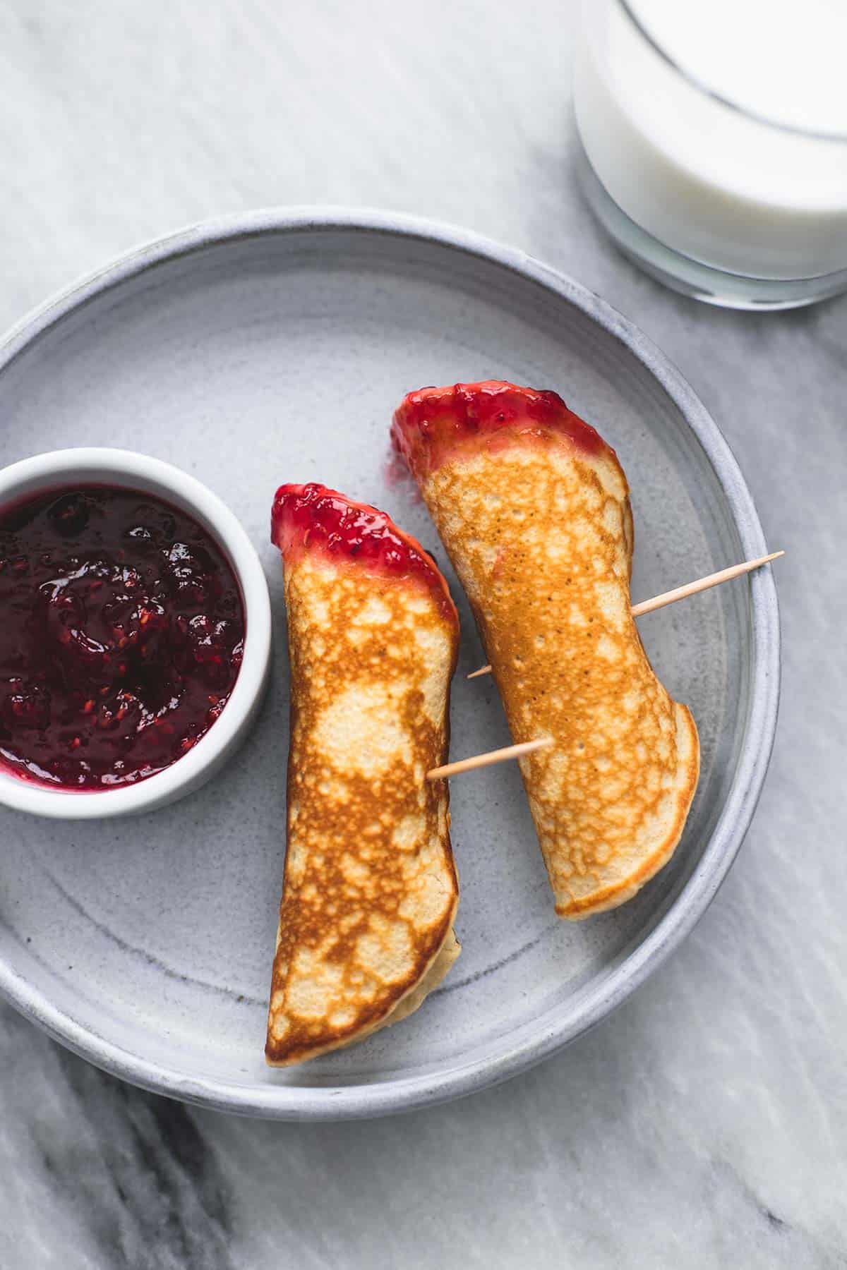 top view of pb & j pancake dippers with a bowl of jelly on the side all on a plate with a glass of milk on the side.