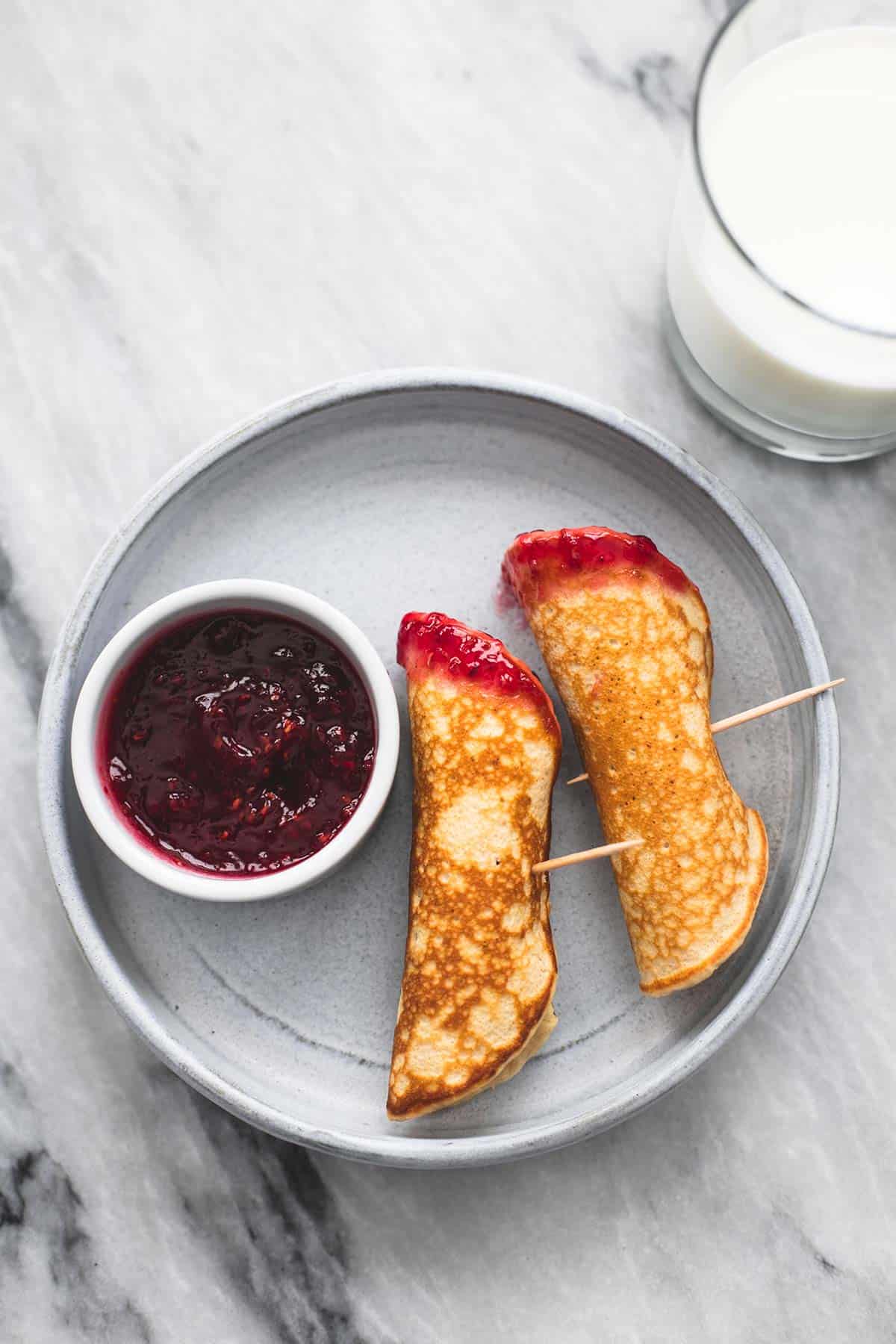 top view of pb & j pancake dippers with a bowl of jelly on the side on a plate with a glass of milk on the side.
