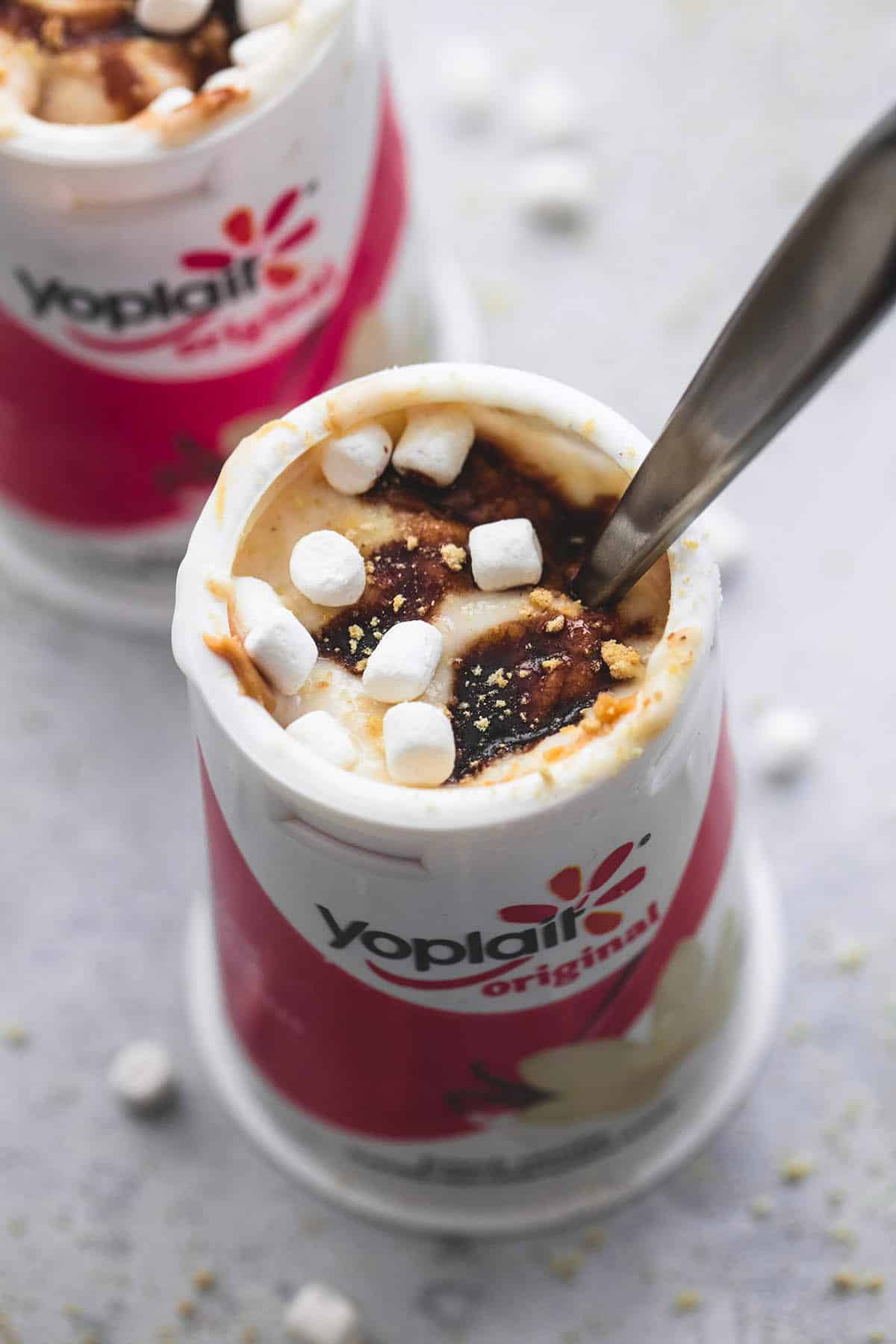 peanut butter s'mores yogurt with a spoon in a Yoplait container with another yogurt on the side.