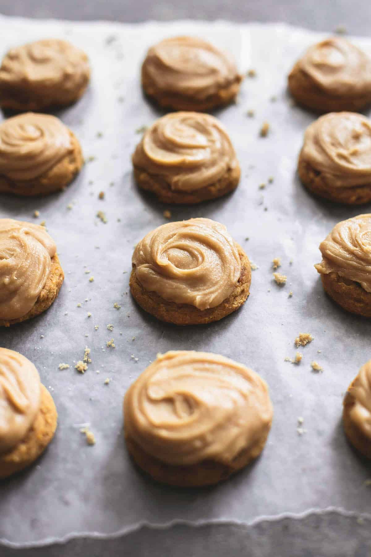 pumpkin cookies with brown sugar frosting in vertical lines on wax paper.