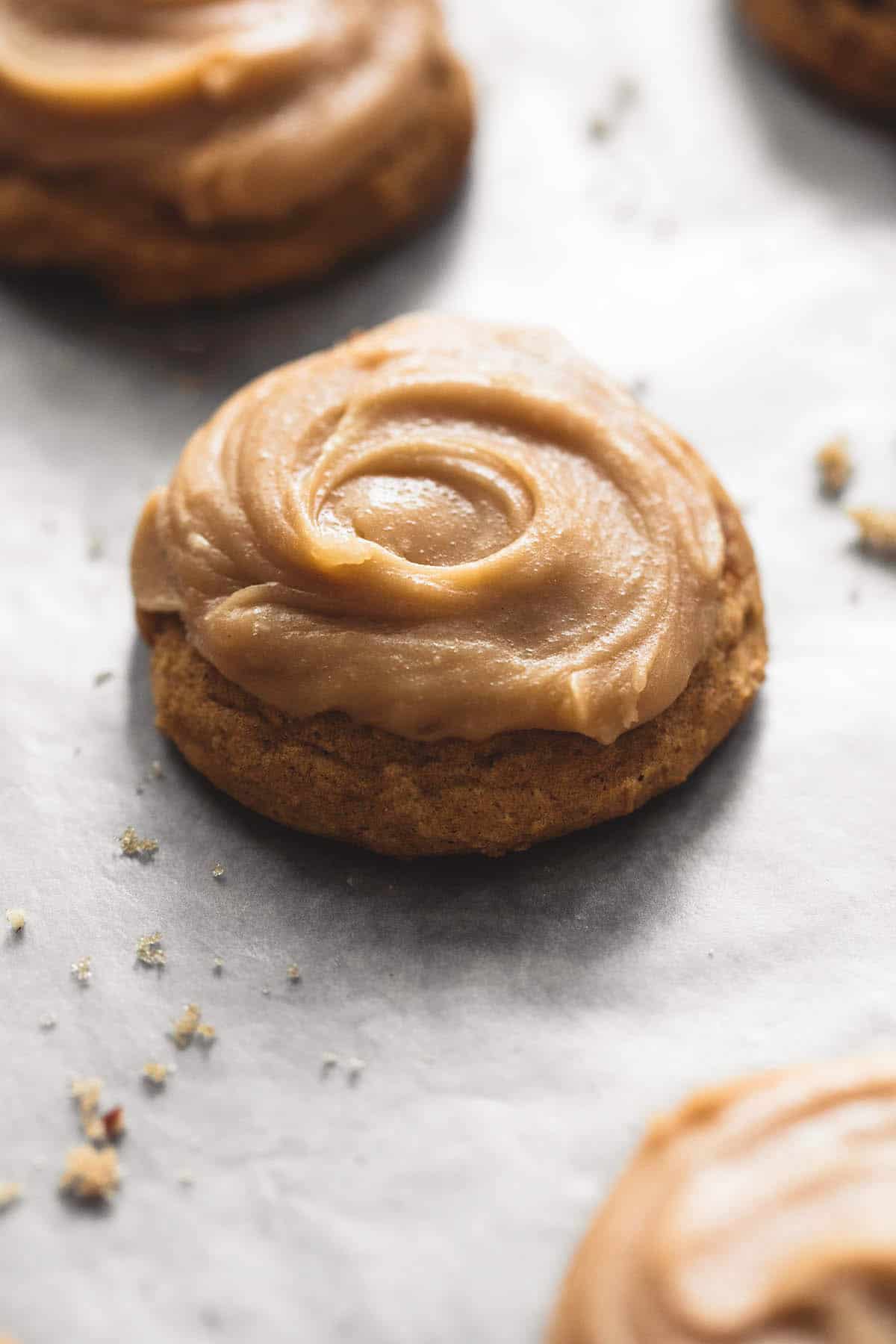 a pumpkin cookie with brown sugar frosting with more cookies on the side.