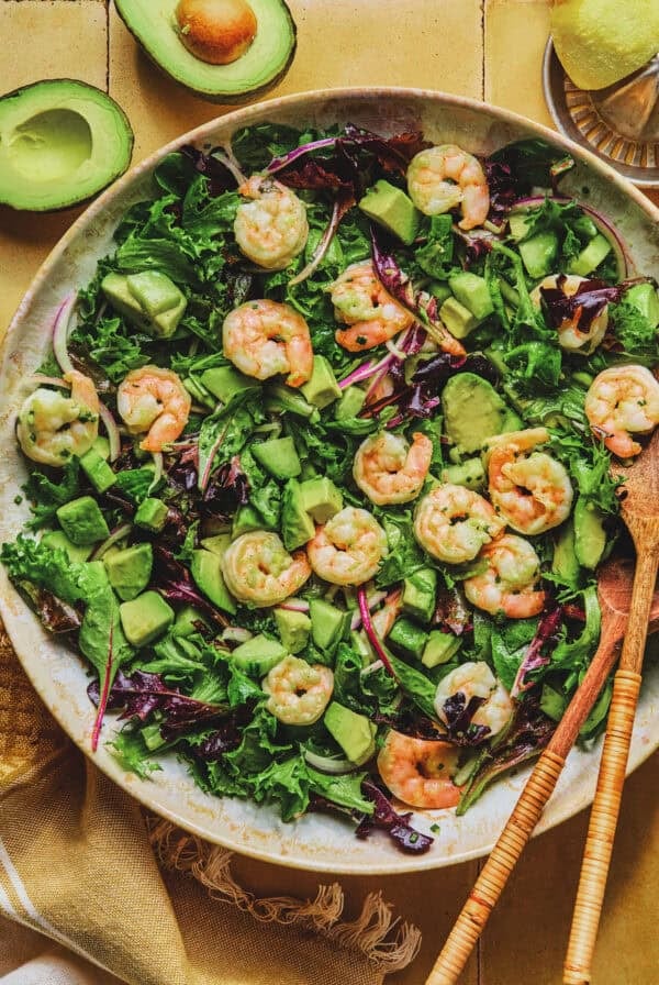 Overhead of shrimp avocado salad with wooden serving spoons in a bowl.