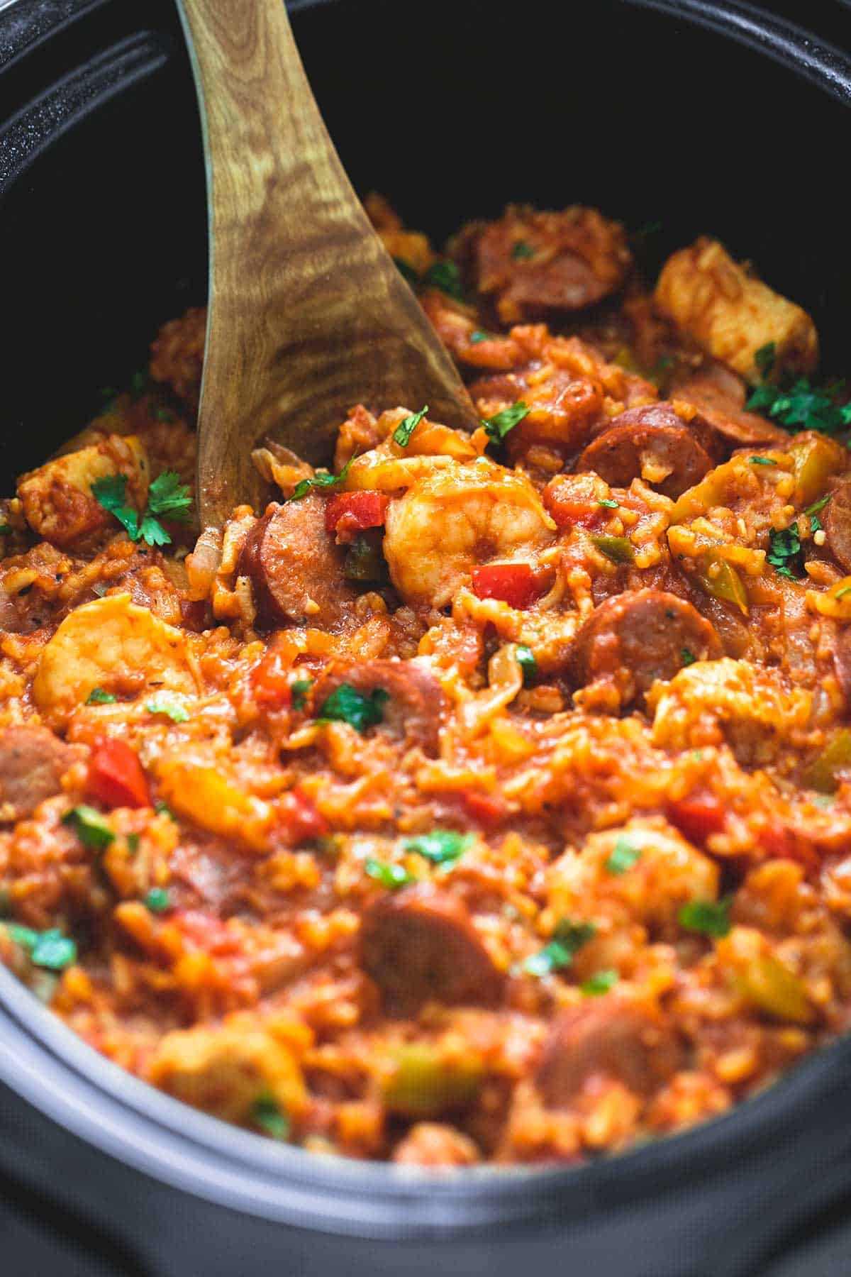 slow cooker jambalaya and a wooden serving spoon in a slow cooker.