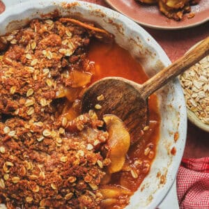 Overhead of apple crisp and a serving spoon in a serving dish with a scoop missing.