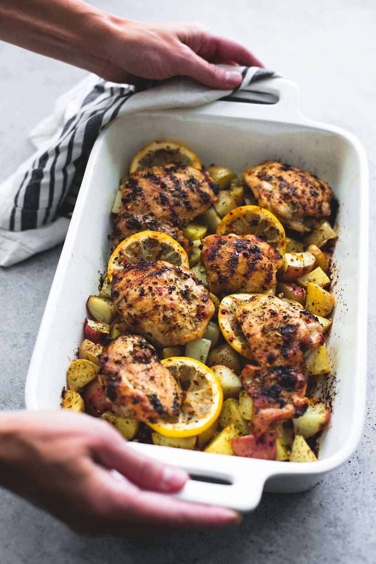 hands holding an oven pan with baked lemon herb chicken & potatoes in it.