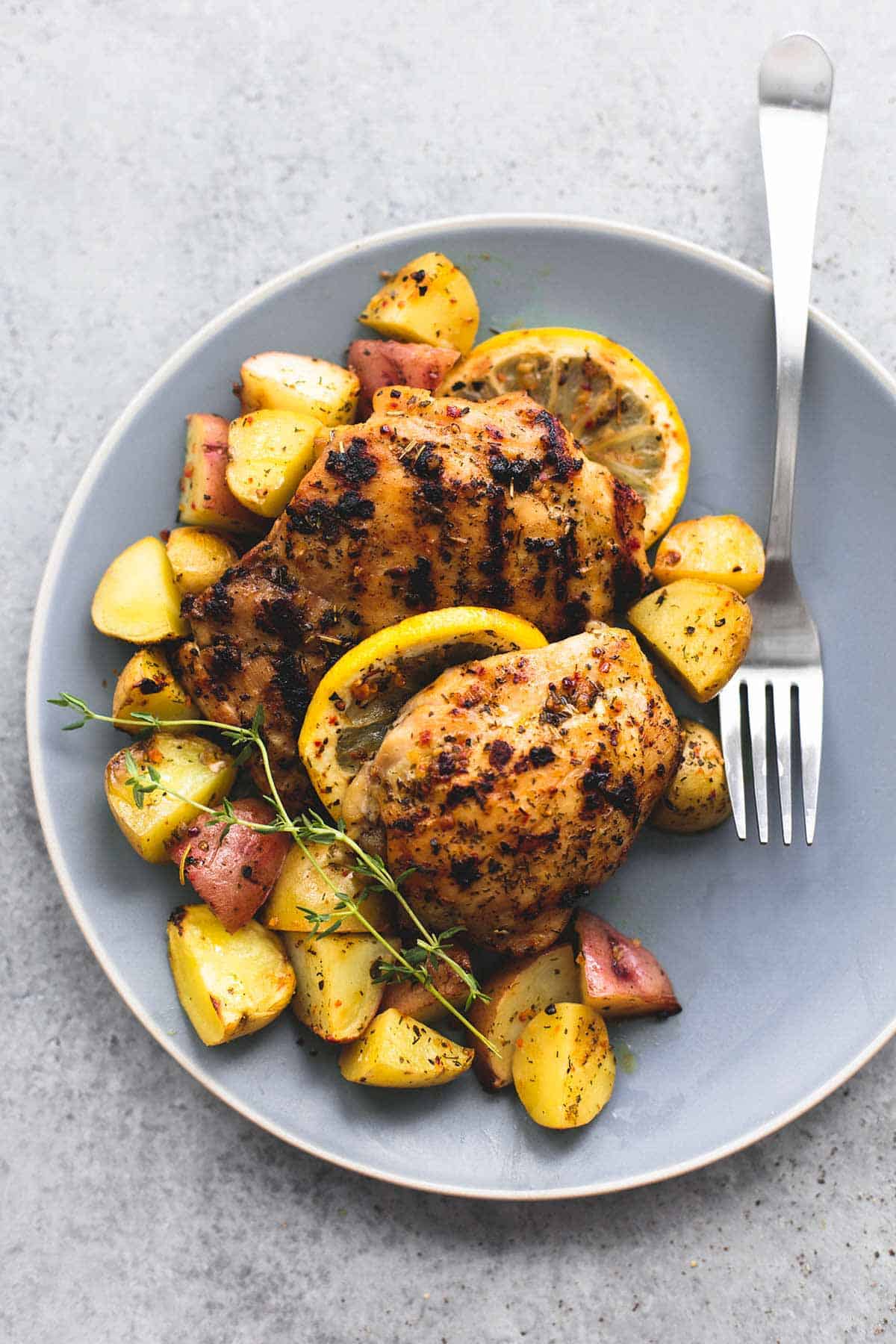 top view of baked lemon herb chicken & potatoes with a fork on a plate.