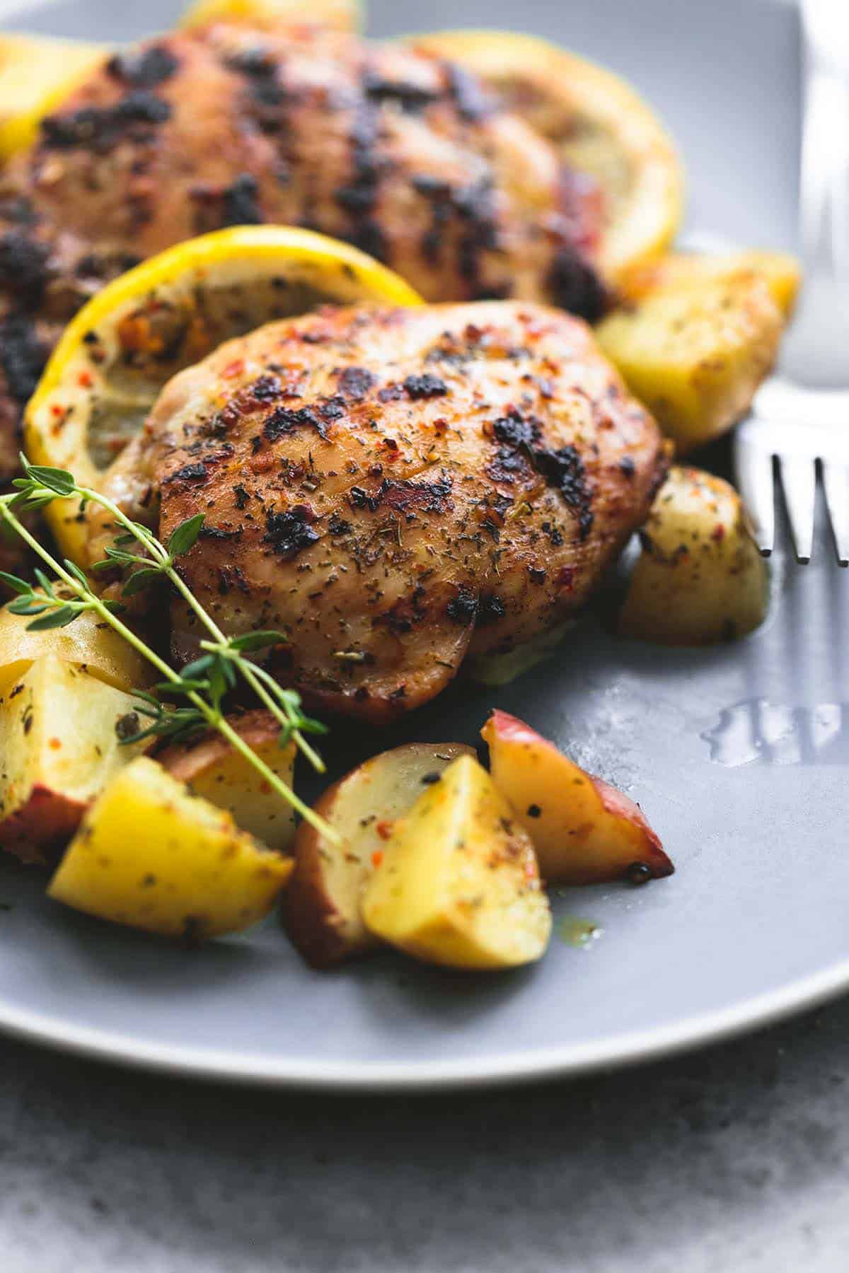 close up of baked lemon herb chicken & potatoes with a fork on a plate.