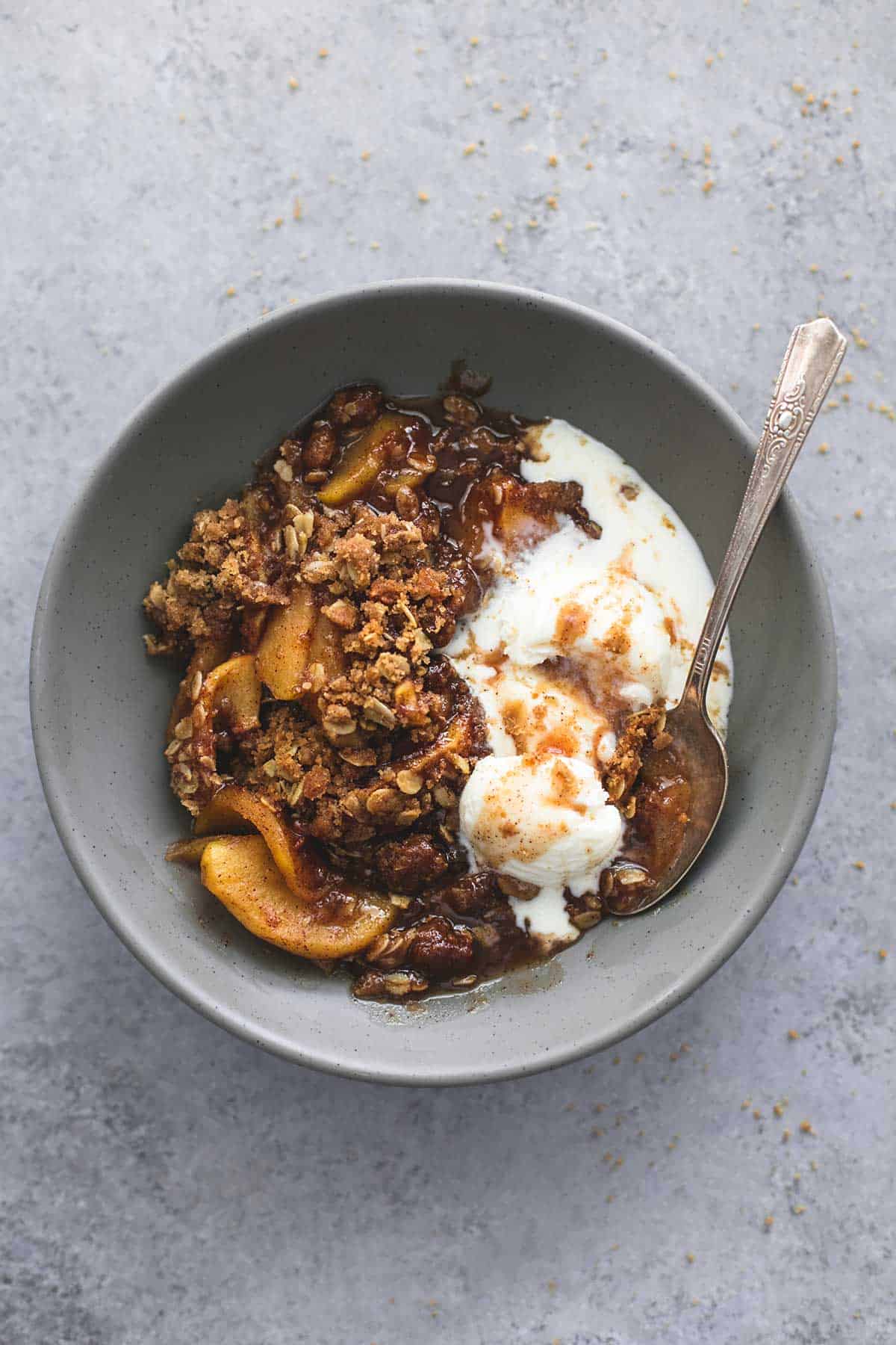 top view of apple crisp with vanilla ice cream and a spoon in a bowl.