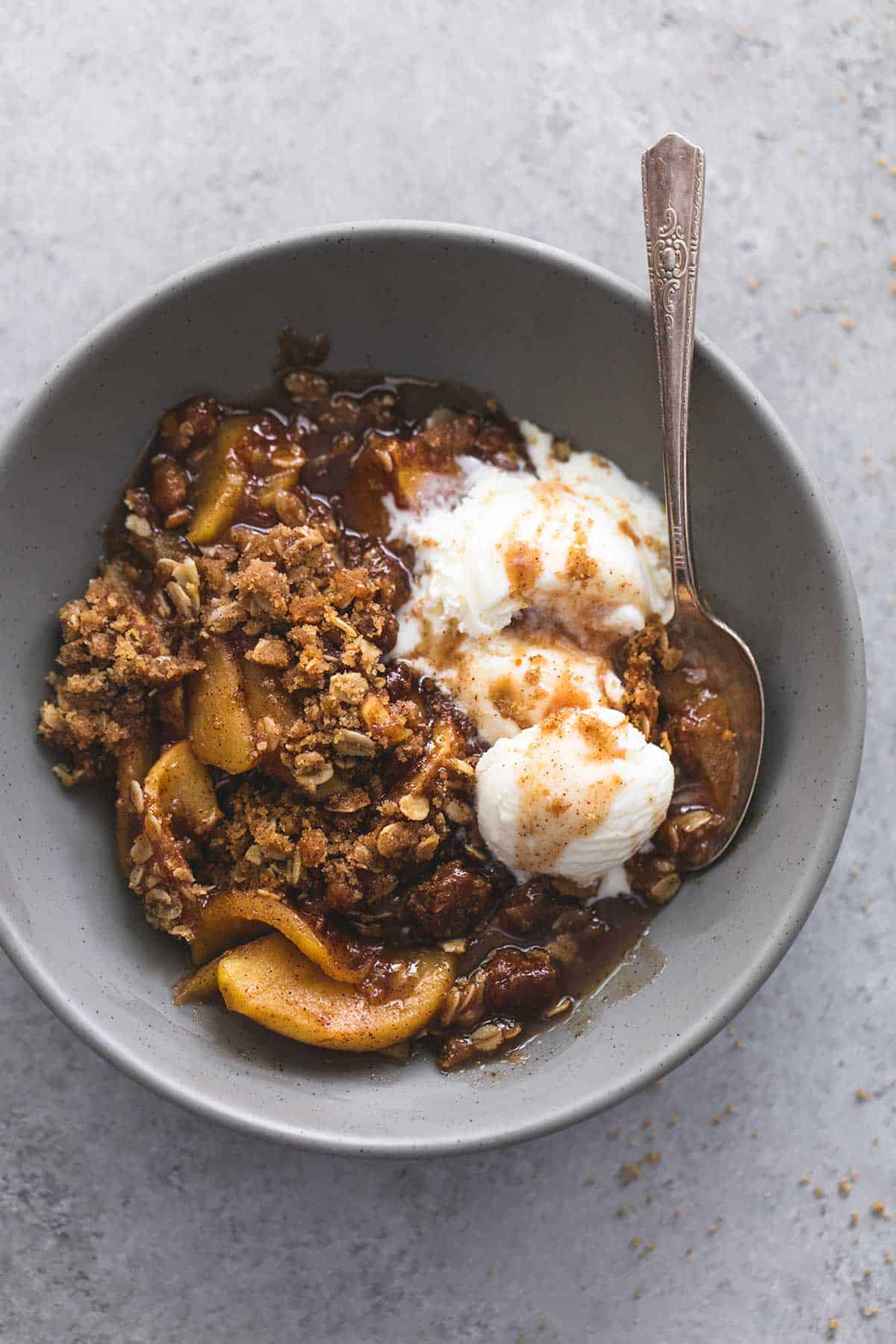 top view of apple crisp with vanilla ice cream and a spoon in a bowl.