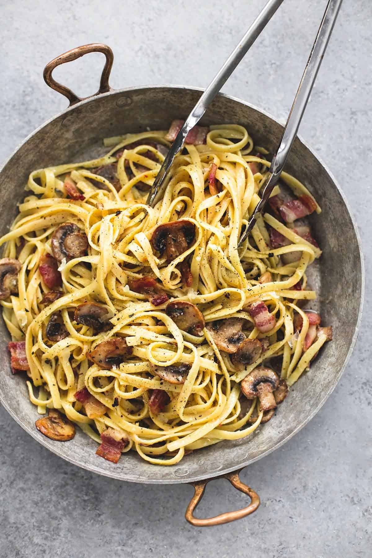 top view of parmesan bacon mushroom fettuccine and tongs in a wok.