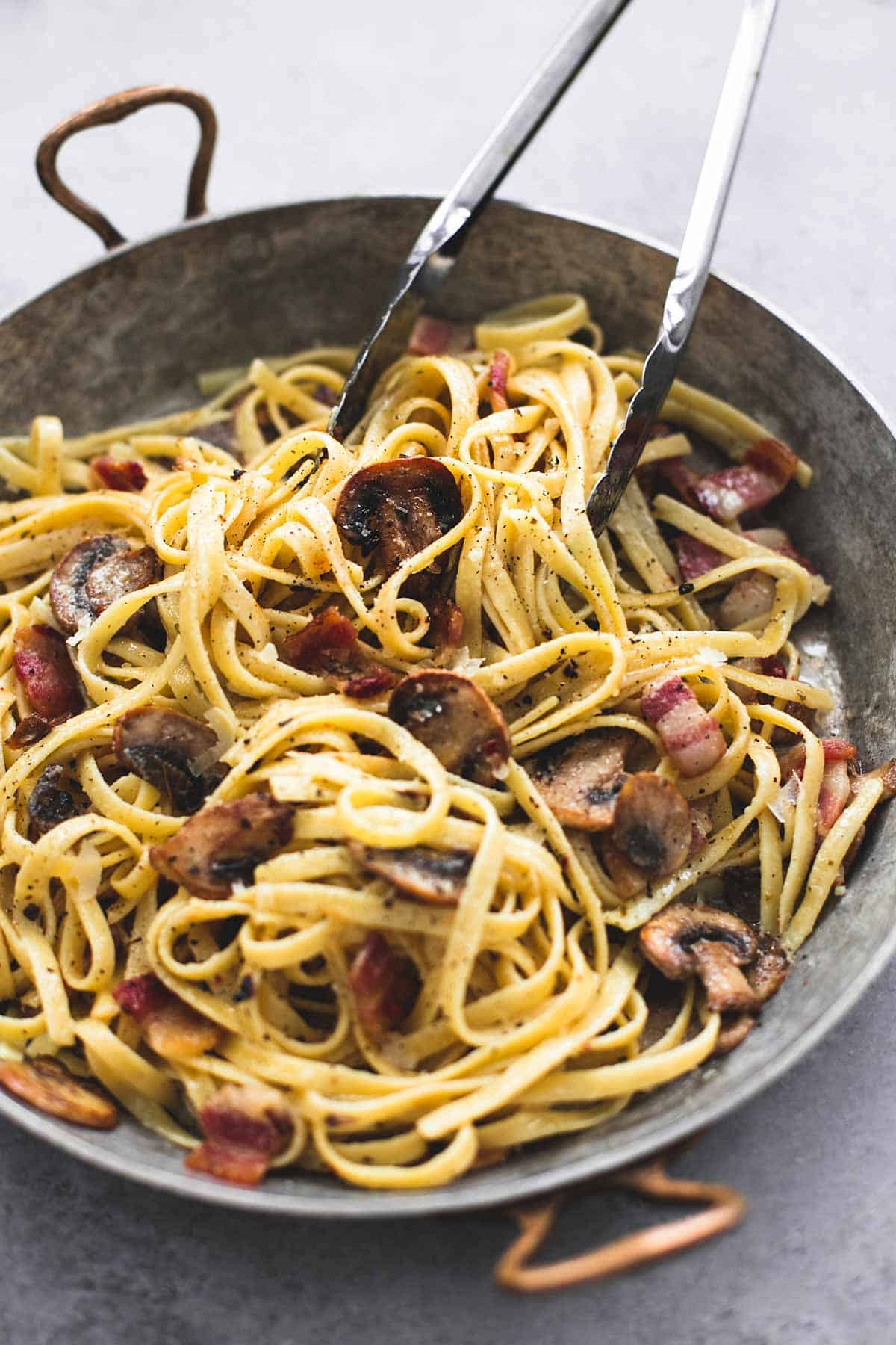 parmesan bacon mushroom fettuccine with tongs in a wok.