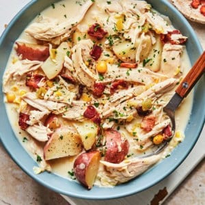 spoon digging into bowl of soup with corn, chicken, potatoes, and corn.