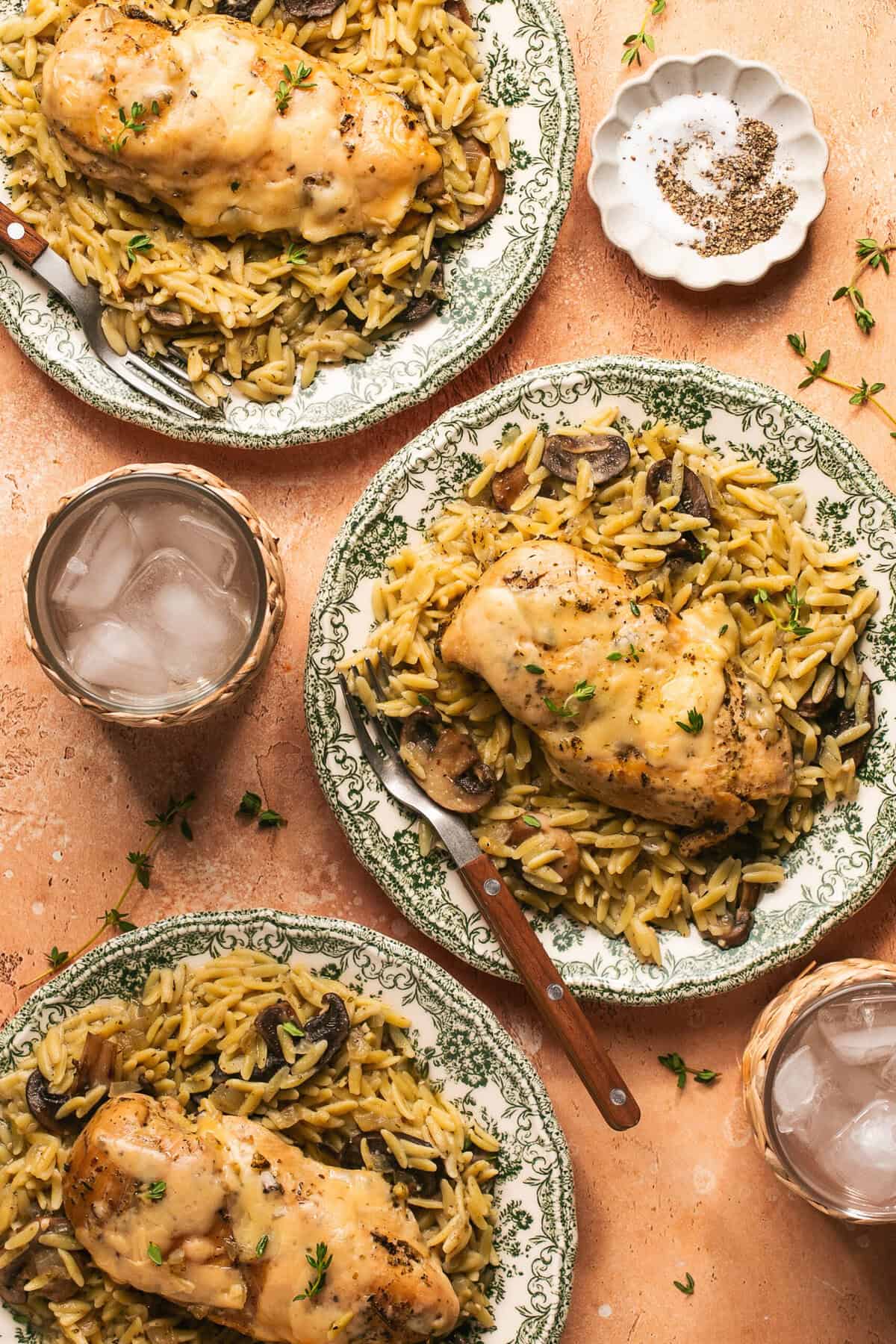 Overhead of plates of slow cooker parmesan herb chicken and orzo next to cups of water.