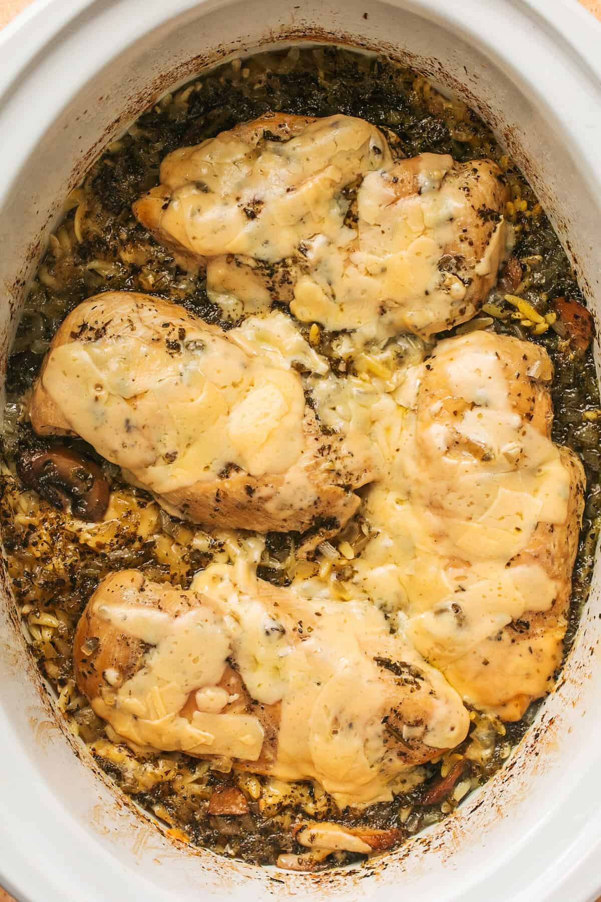 Overhead of slow cooker parmesan herb chicken and orzo in a slow cooker.