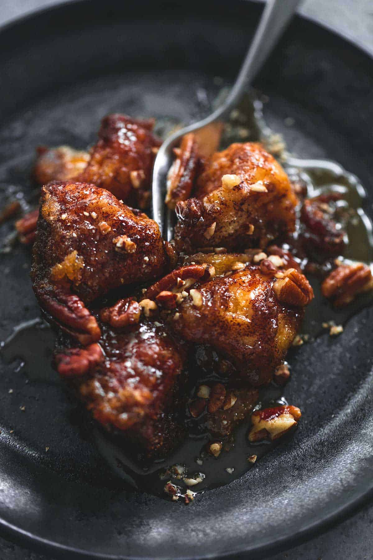 close up of a fork cutting into slow cooker caramel pecan monkey bread on a plate.