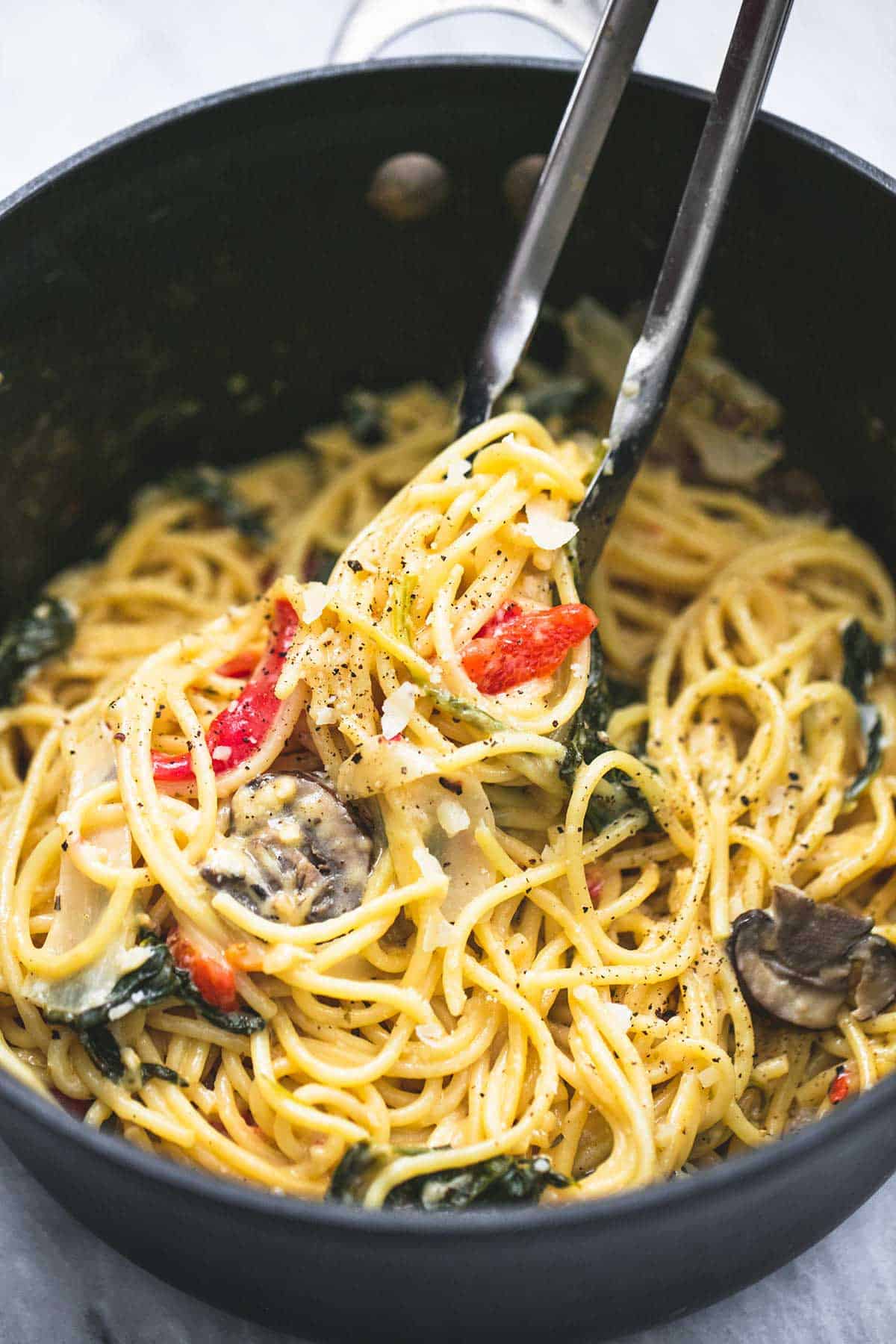 close up of tongs picking up some creamy Tuscan garlic spaghetti form a pan.